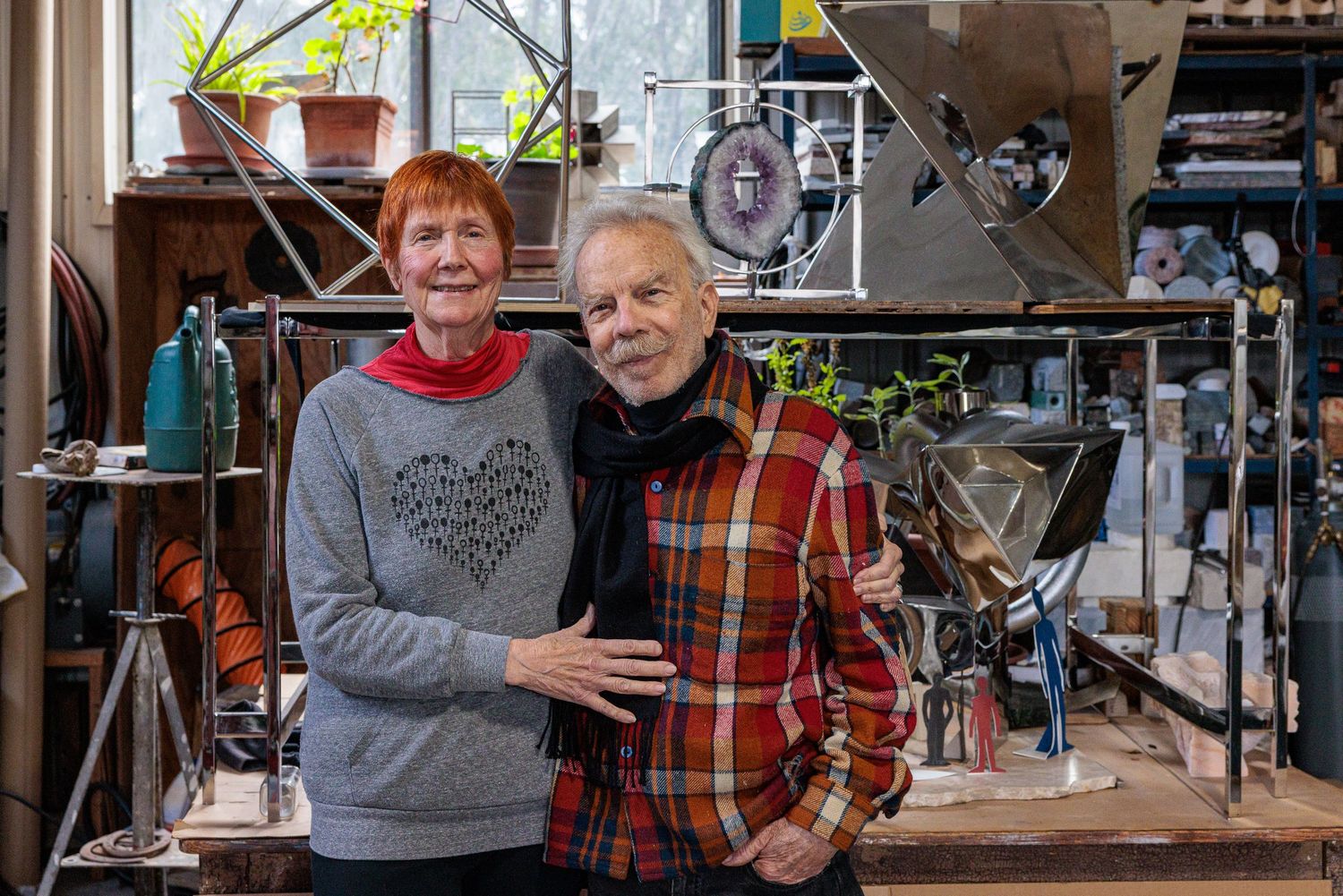 Two people standing together in a workshop surrounded by tools and equipment
