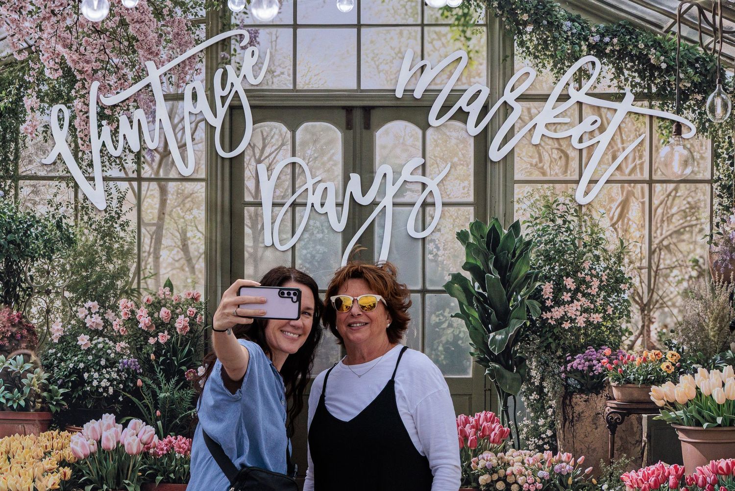 Two women taking a selfie in front of the Vintage Market Days flower booth backdrop Xenia Ohio