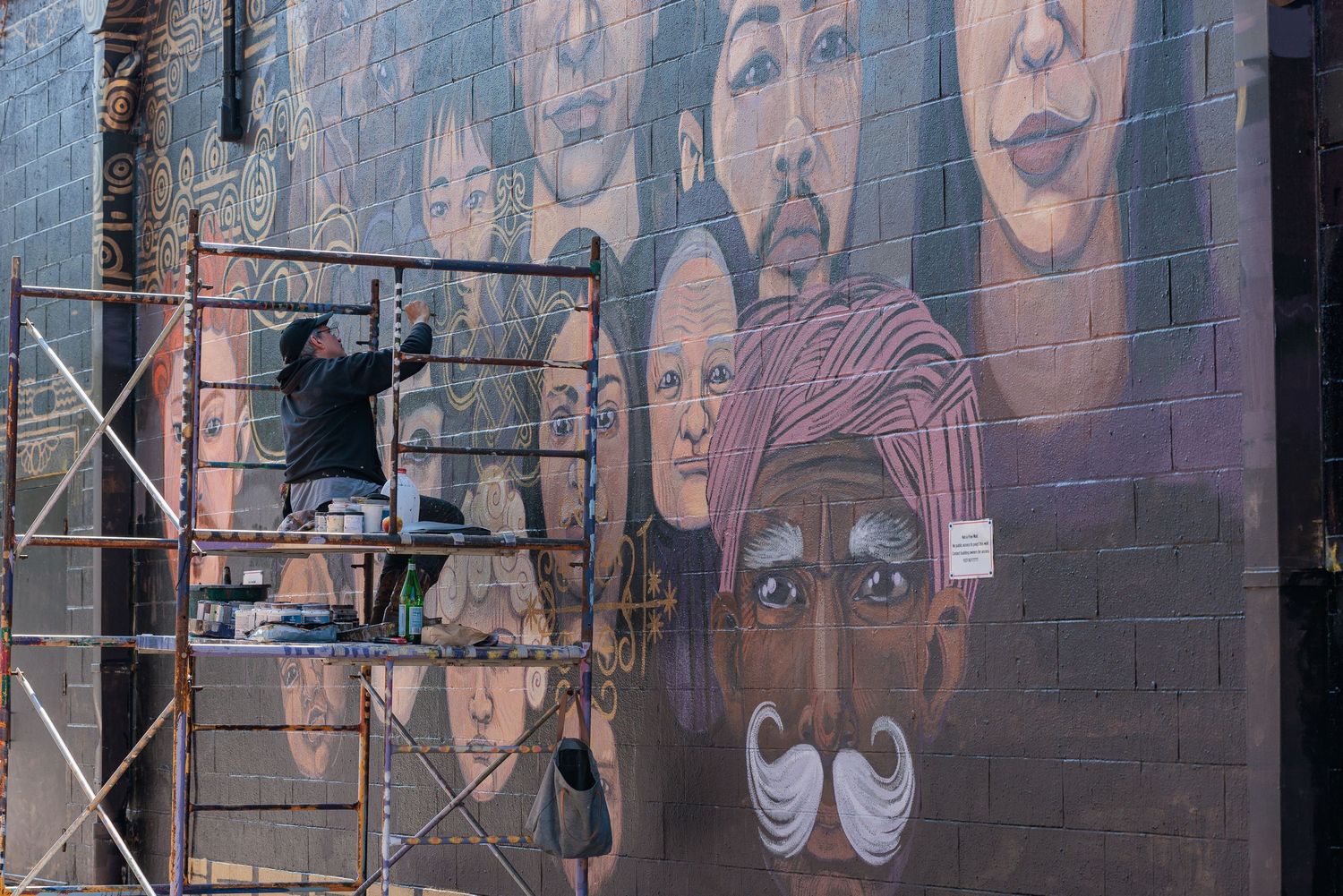 Muralist Pierre Nagley painting on scaffolding, close view of brushwork on a large-scale mural