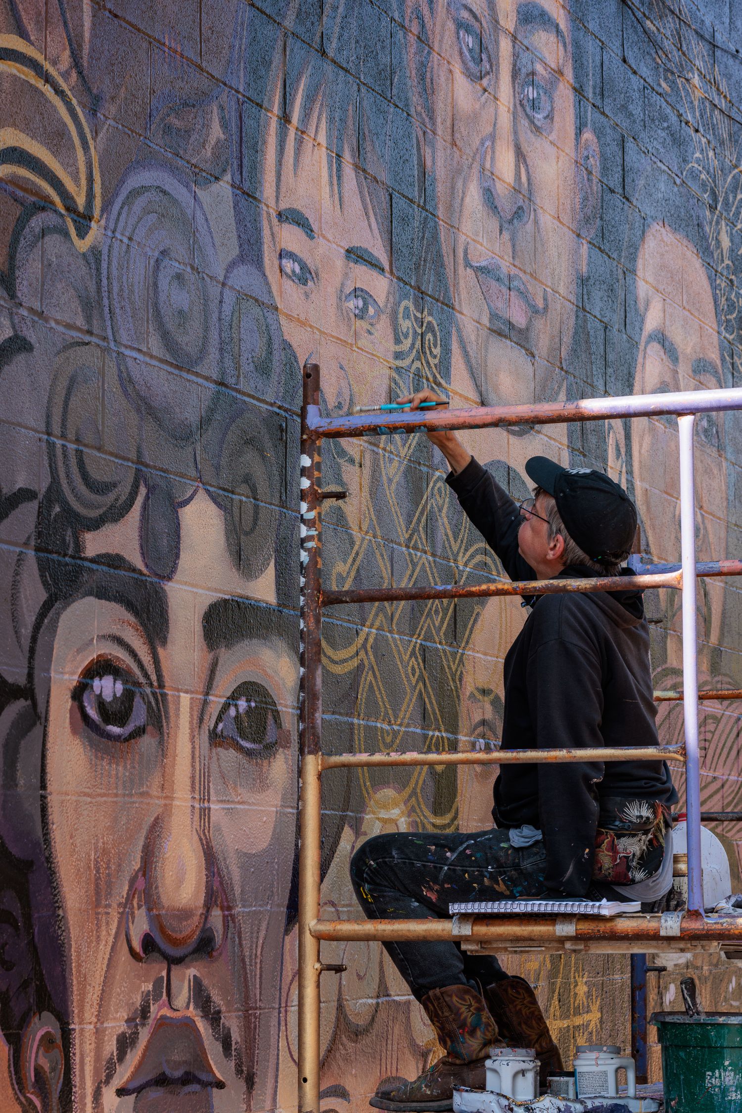 Vertical view of Muralist Pierre Nagley on scaffolding painting a large portrait face on a mural