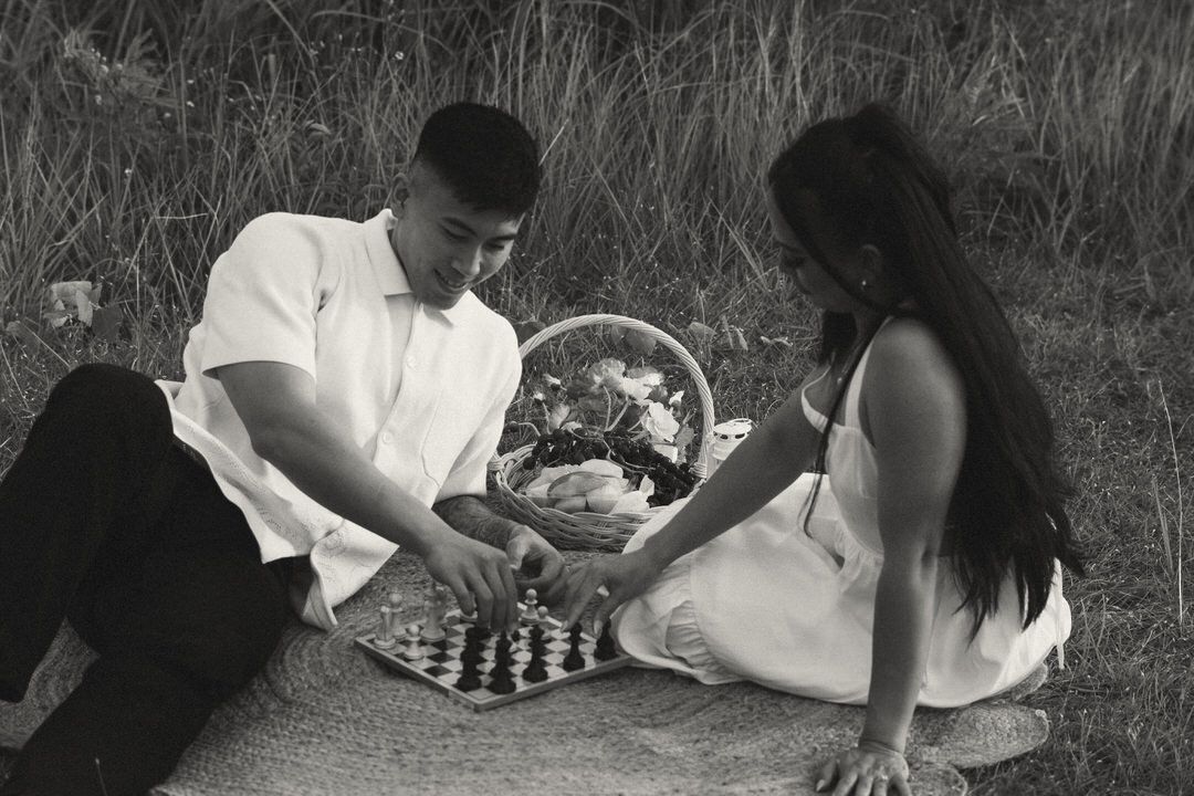Couple playing chess on a blanket during a romantic outdoor picnic in a field, black and white photo.