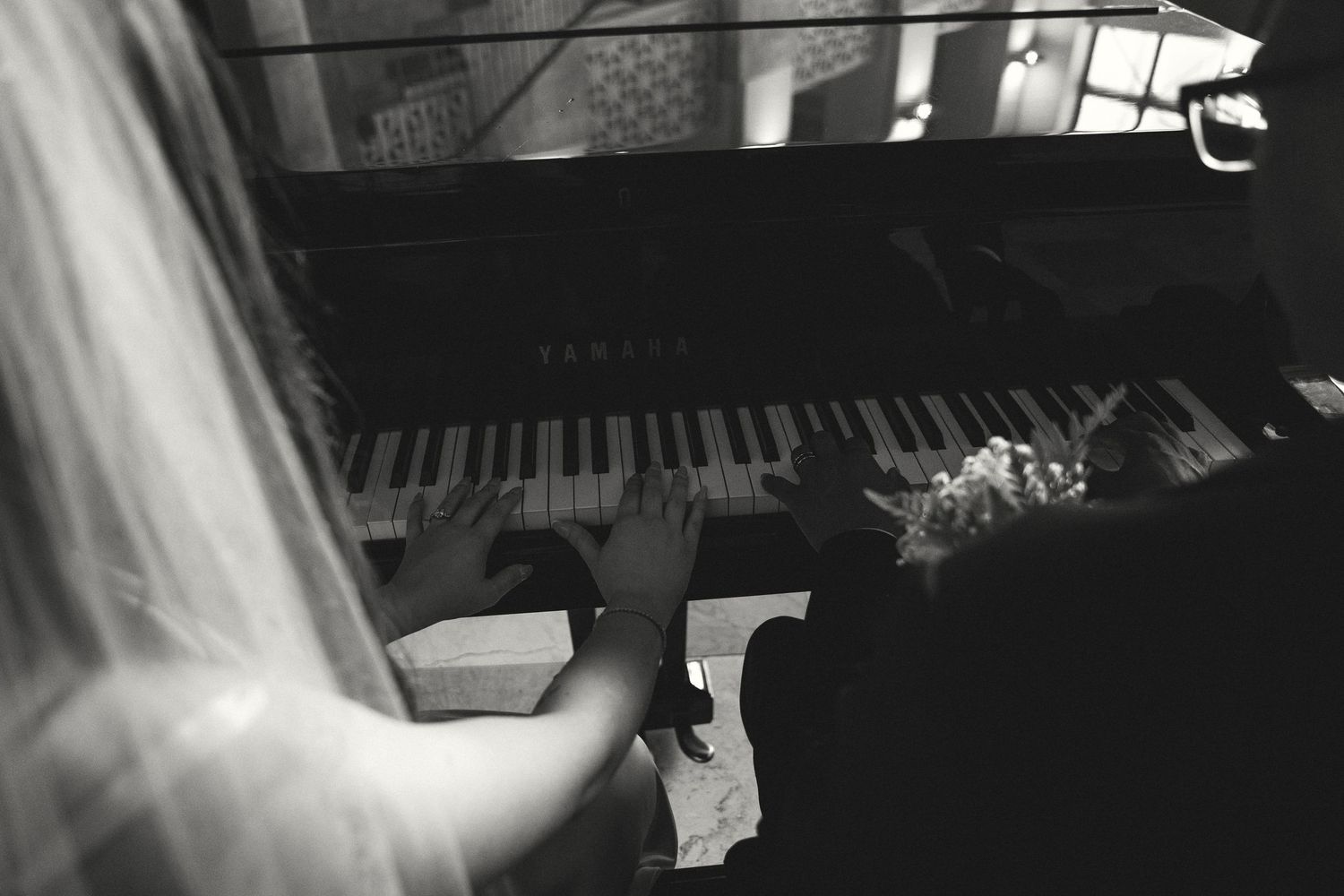 Bride and groom playing a Yamaha grand piano together at their wedding reception in black and white.