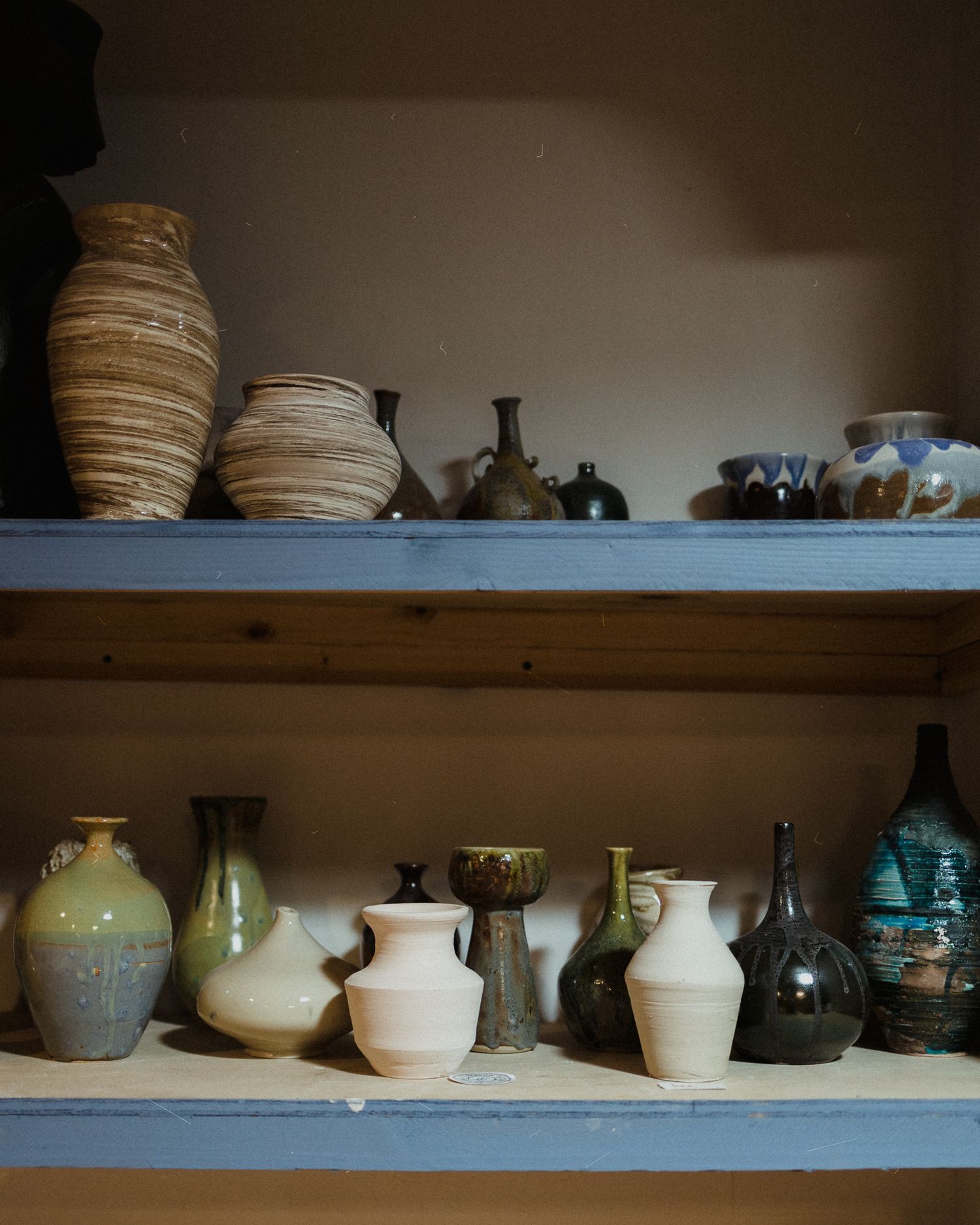 Two wooden shelves display a collection of handmade ceramic vases and pottery in earthy tones inside a rustic cabinet.