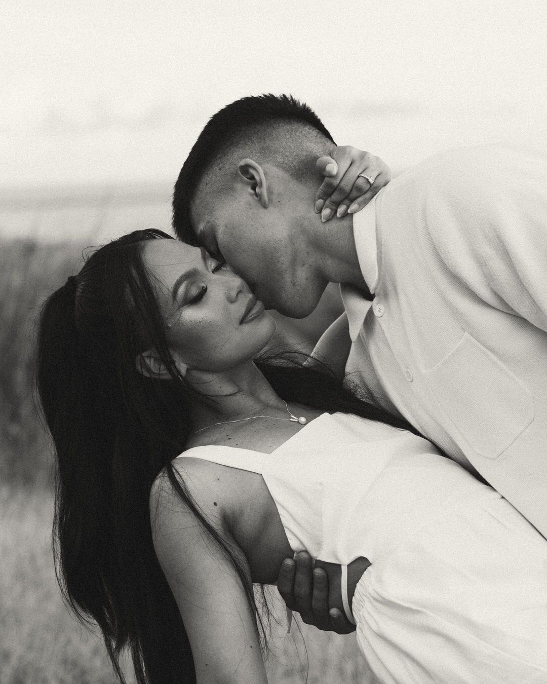 Black and white photo of a couple sharing a romantic kiss outdoors, the man dipping the woman back gently.