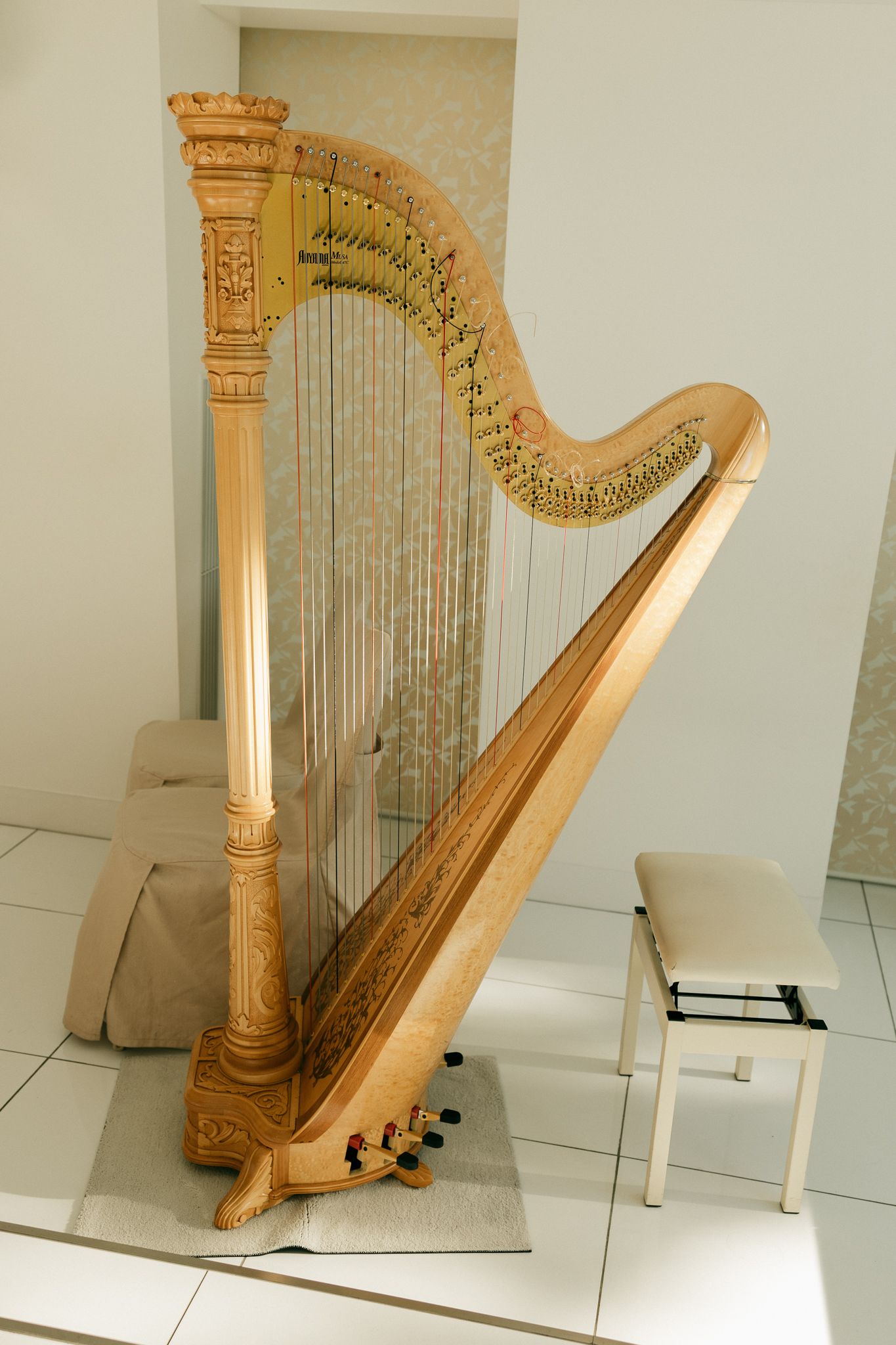 Elegant gold concert harp with ornate carvings stands beside a white bench in a bright, modern room.