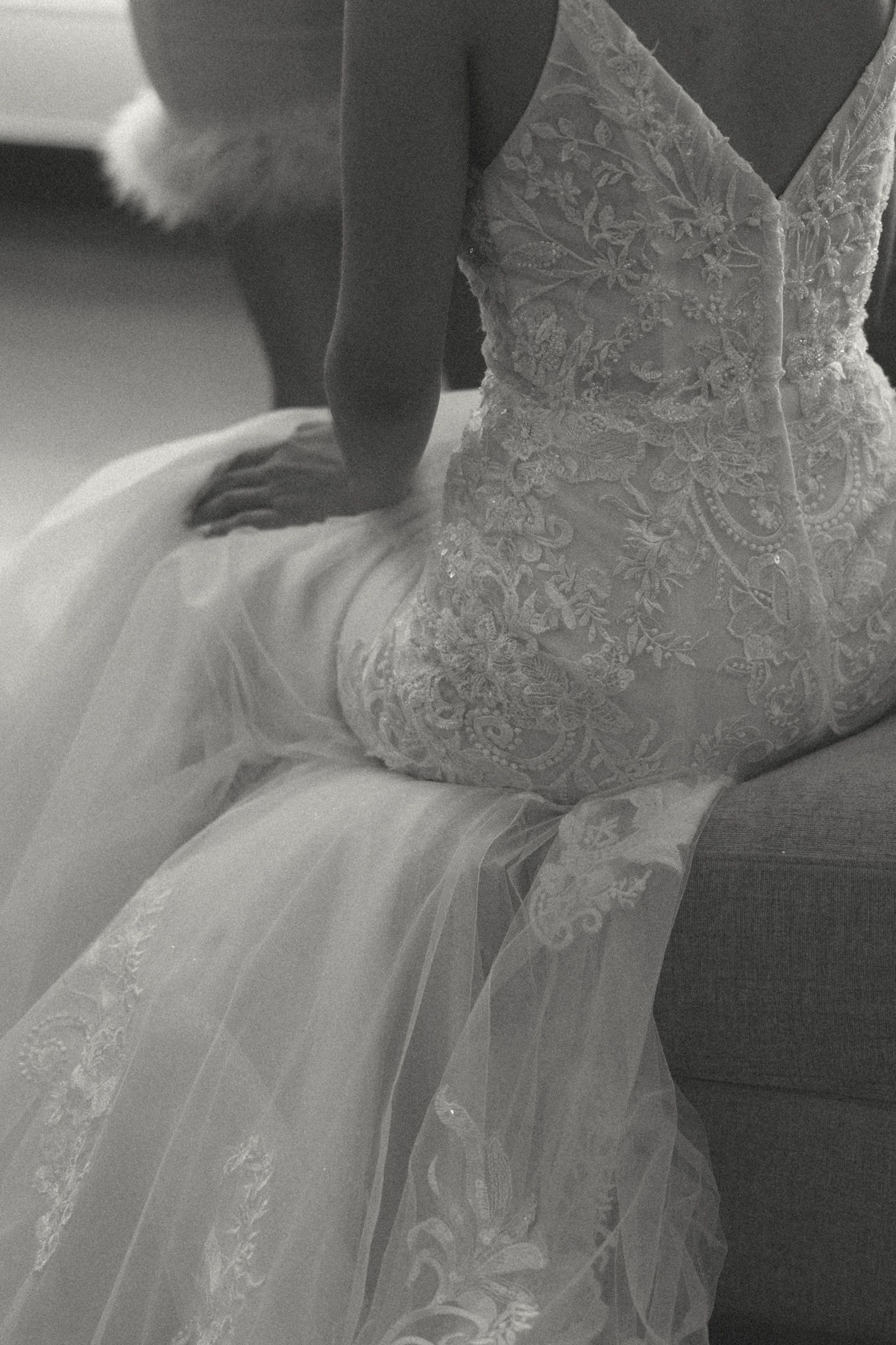 Black and white image of a bride in a fitted lace mermaid wedding gown seated on a sofa.