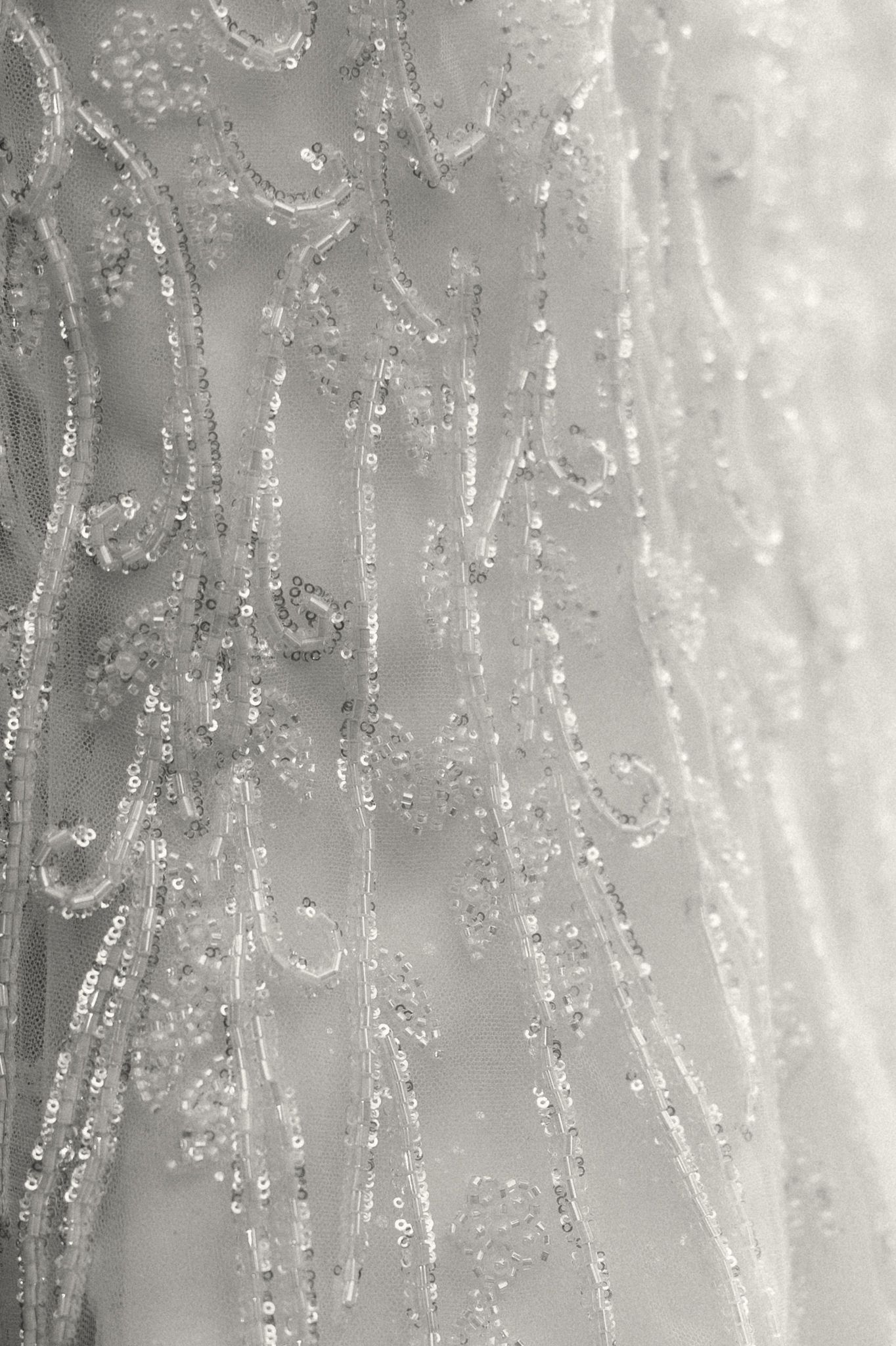 Close-up black and white detail of heavily beaded and sequined wedding gown fabric with floral motifs.