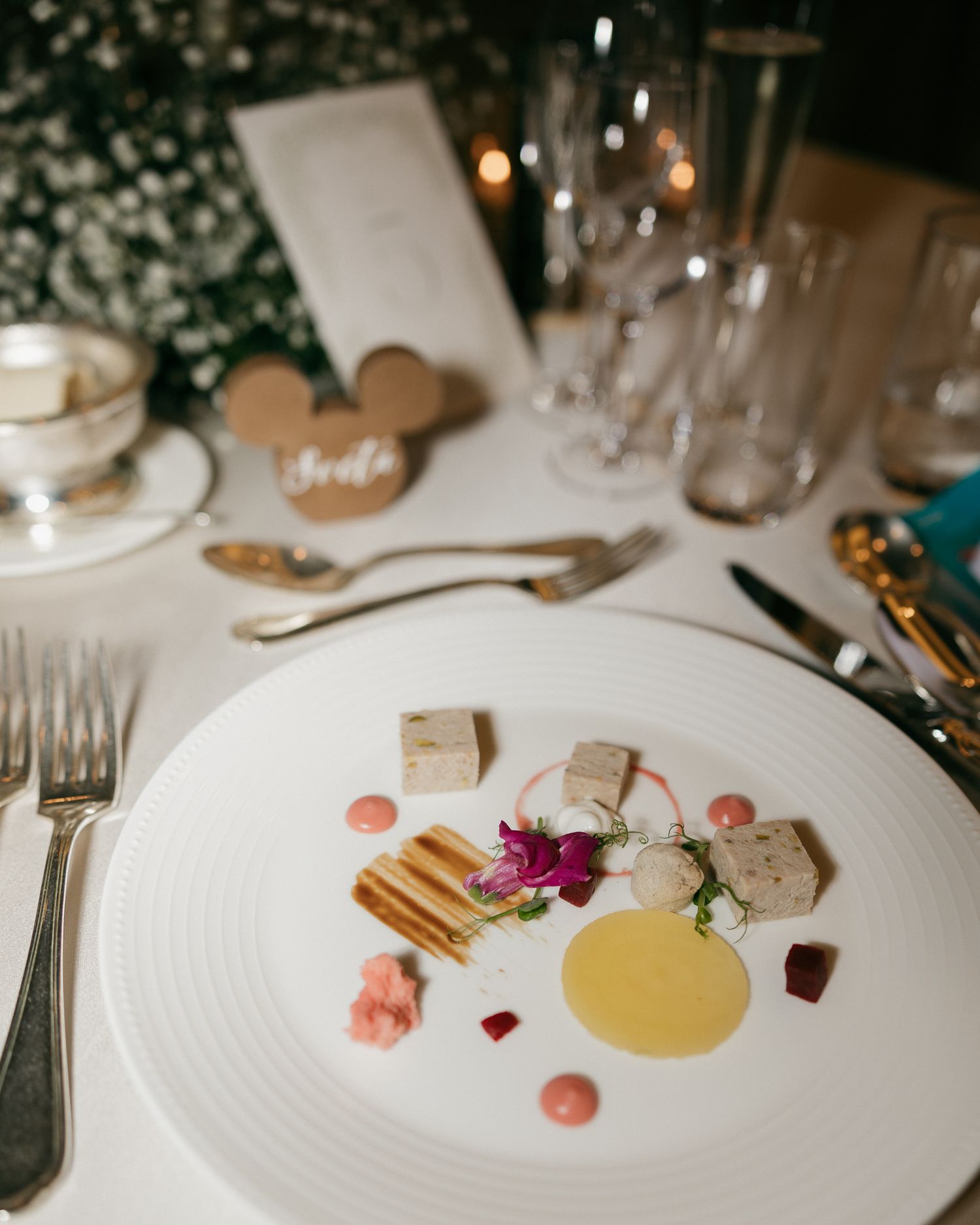 Elegant fine dining plate with artisan terrine, edible flowers, and sauce dots on white plate at a wedding reception.