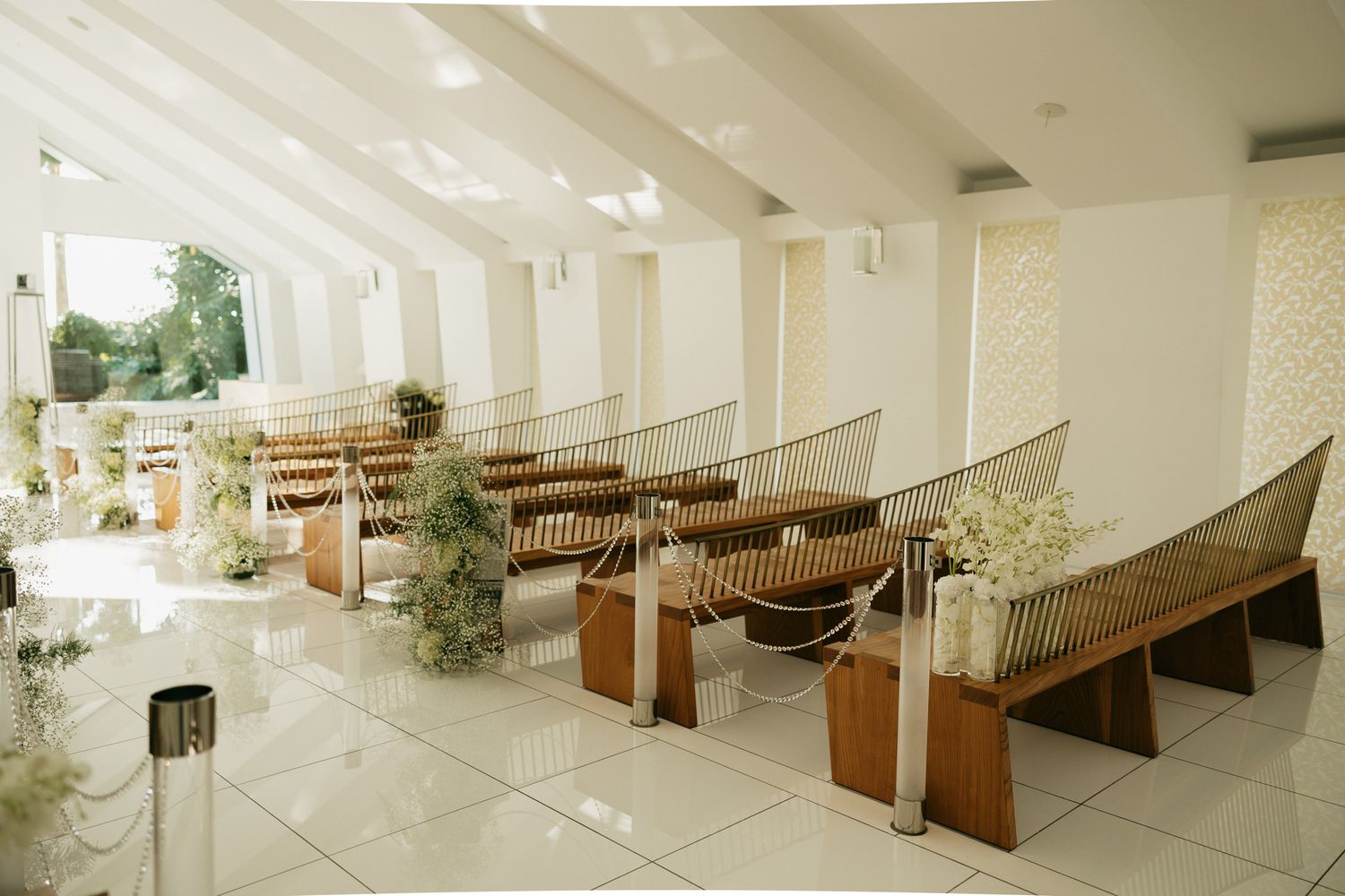 Elegant wedding chapel interior with wooden pews, white walls, and floral arrangements lining the aisle.