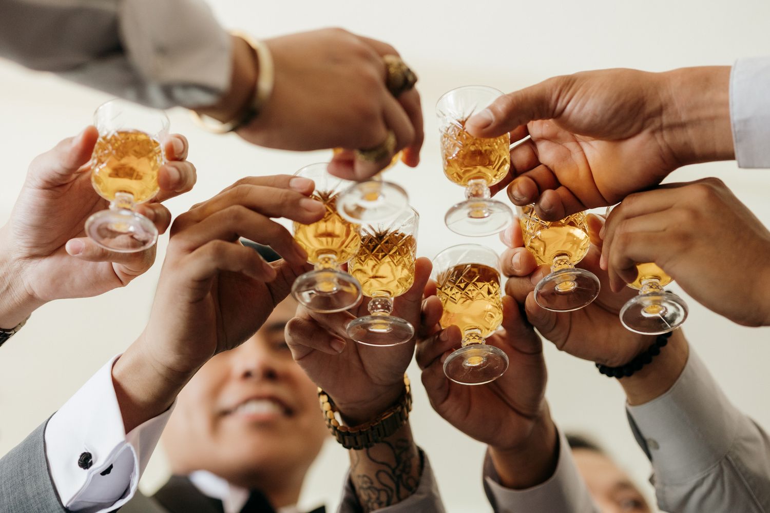 Group of men in suits toasting with glasses of whiskey or bourbon in a celebratory cheers gesture.