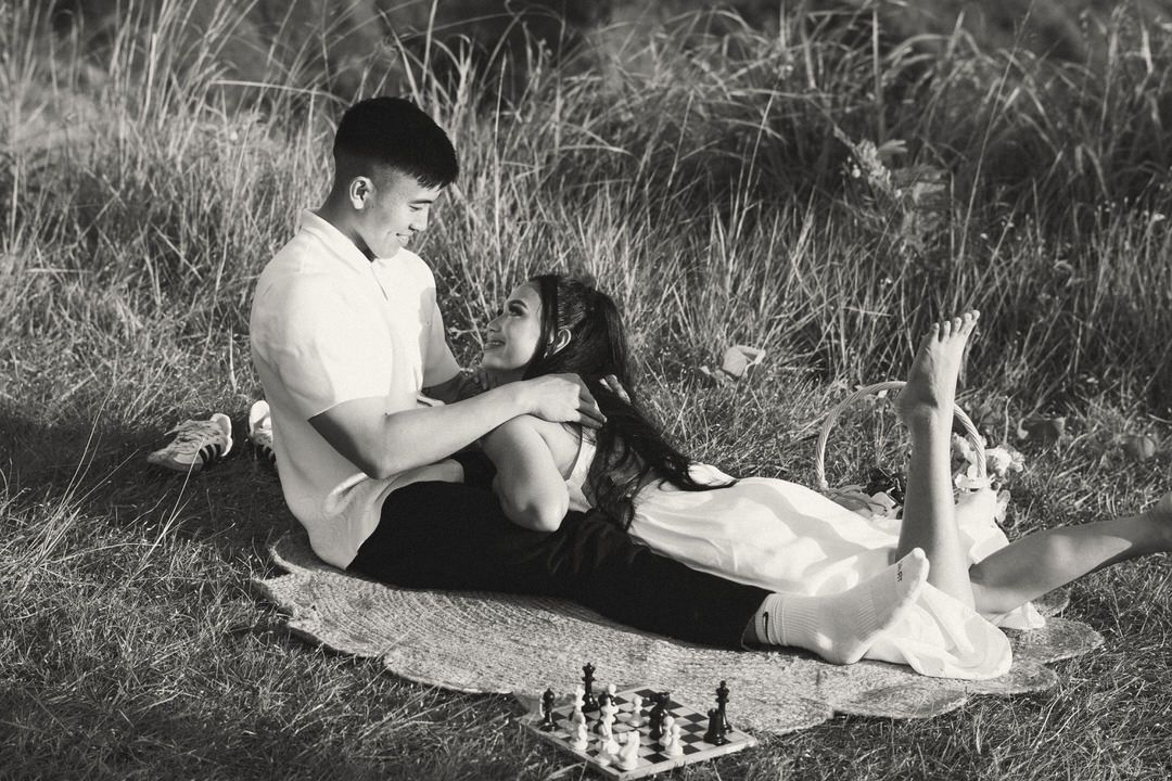 Couple relaxing on a blanket outdoors with a chess board nearby in black and white photo.