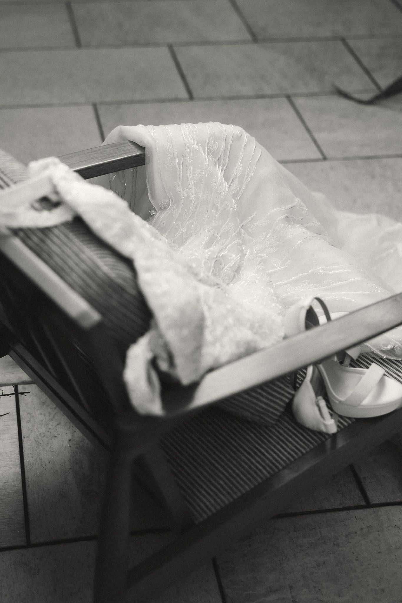 Black and white photo of a wooden baby cradle with plastic lining and white fabric on tiled floor.