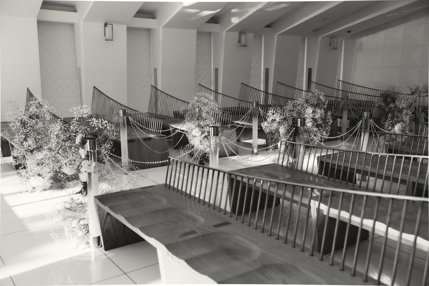 Black and white photo of an elegant indoor space with floral arrangements along railed balconies and tiled floors.