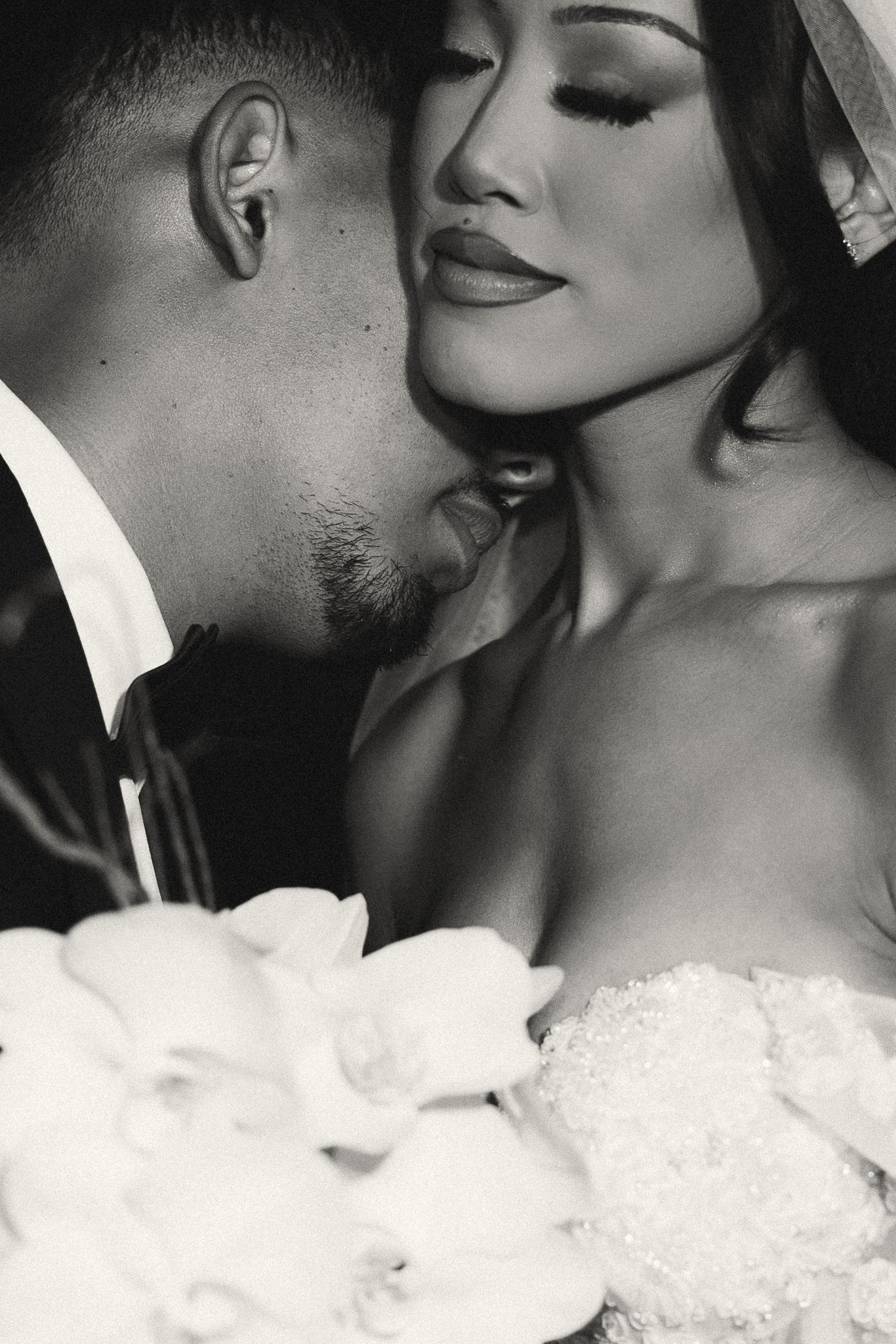 Black and white wedding photo of bride and groom in intimate moment, bride holding white orchid bouquet.