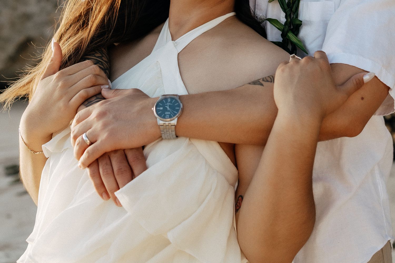 Couple embracing in white outfits, woman wearing a diamond ring and man sporting a blue-faced silver watch.