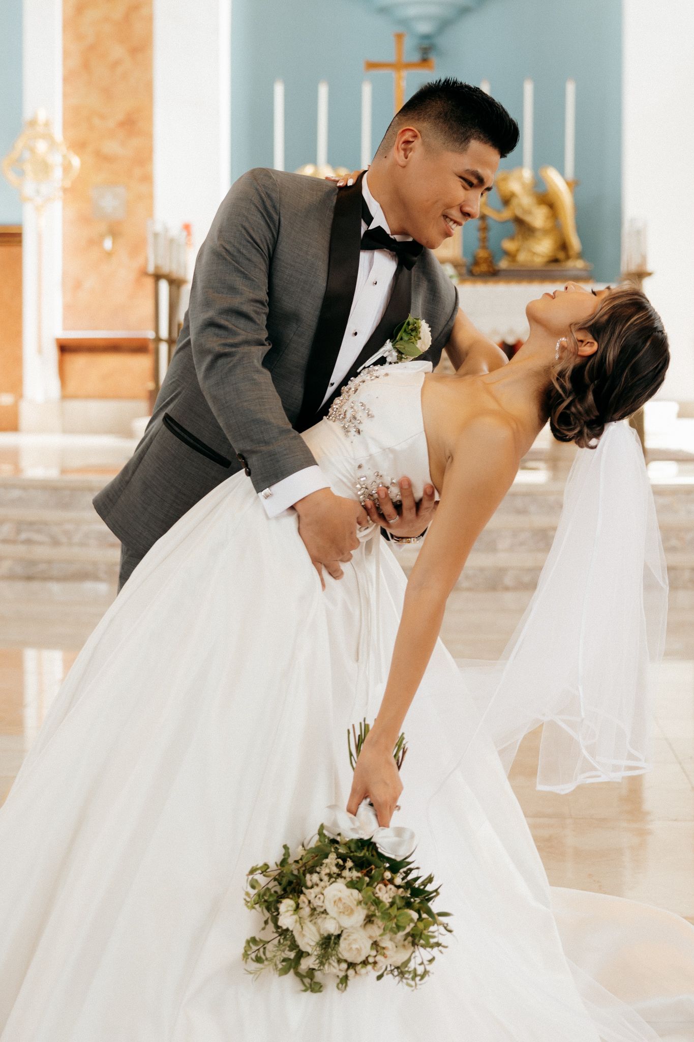 Bride and groom share a romantic dip kiss at church altar, bride in white gown holding bouquet.