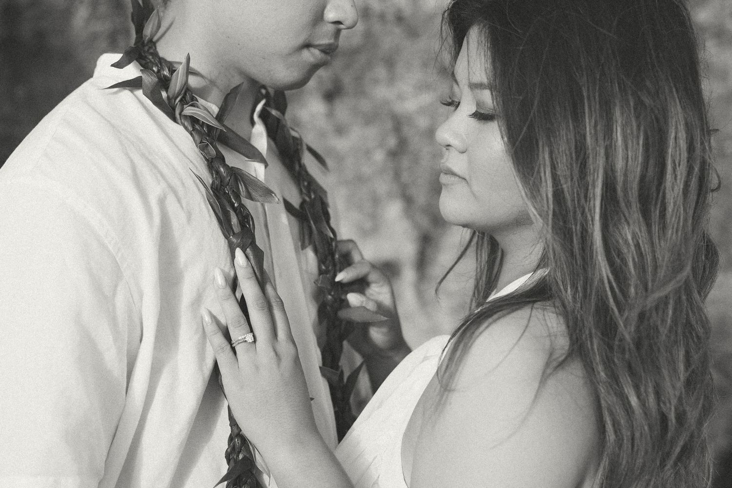 Black and white photo of a romantic couple in an intimate embrace outdoors, woman touching mans chest tenderly.