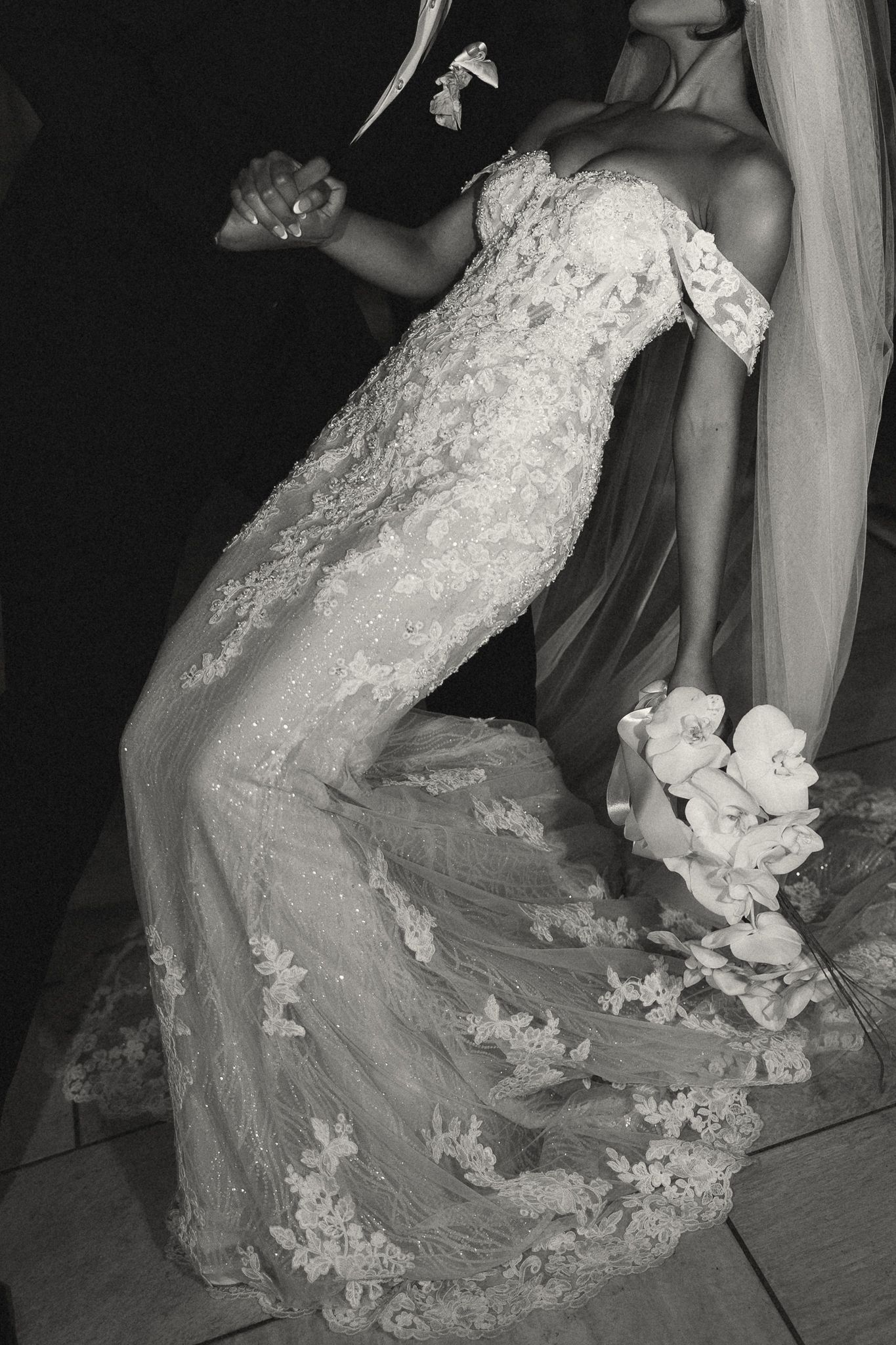 Black and white photo of a bride in a lace mermaid wedding gown holding a floral bouquet while dancing.