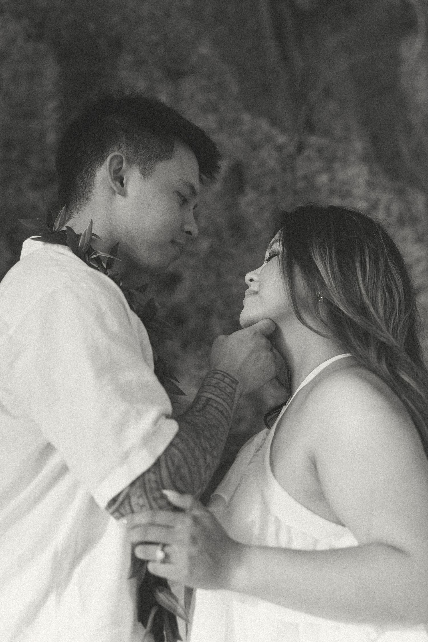 Black and white photo of a couple in white outfits sharing a romantic moment, the man gently lifting the womans chin.