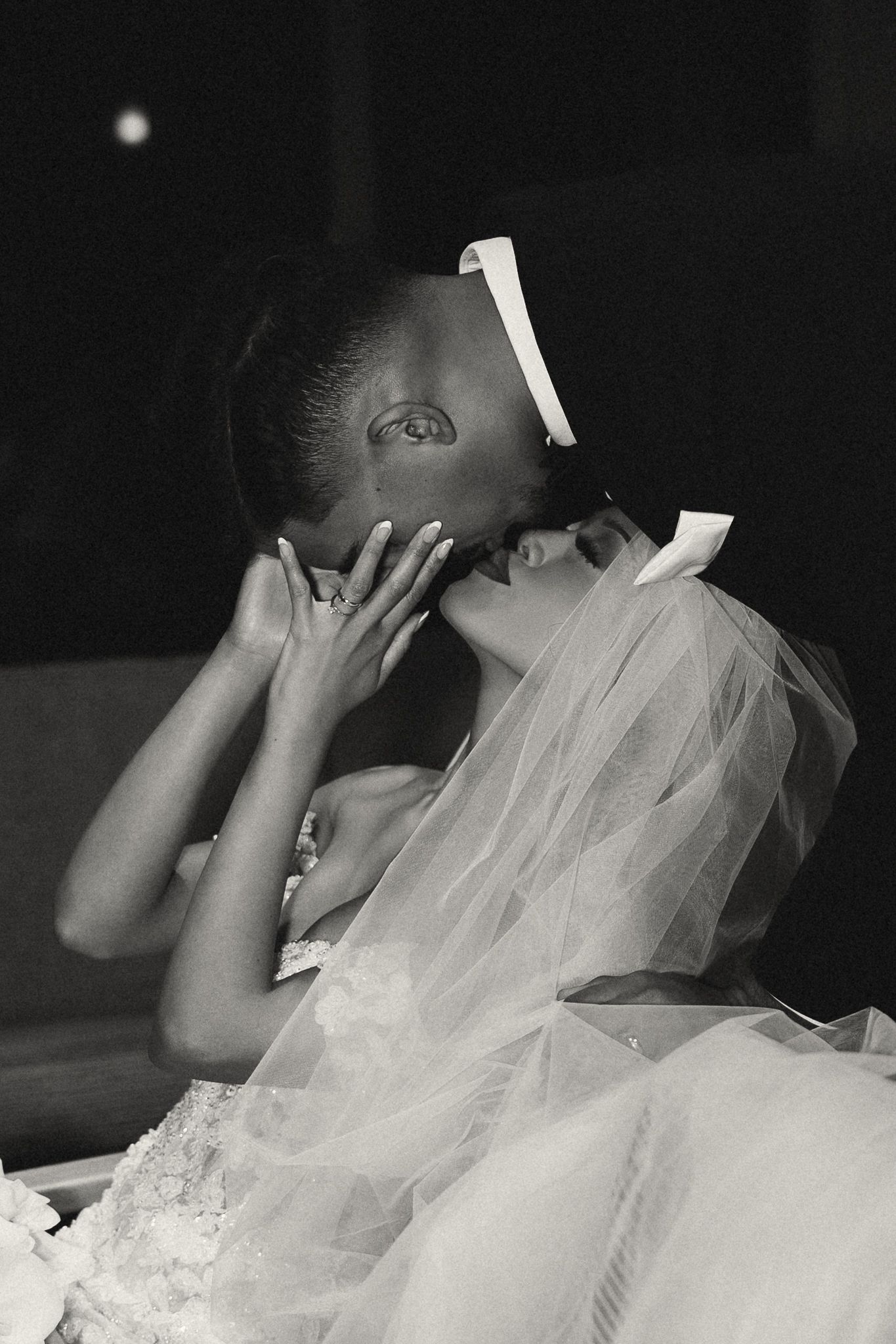 Black and white photo of a bride and groom sharing a romantic first kiss at their wedding ceremony.