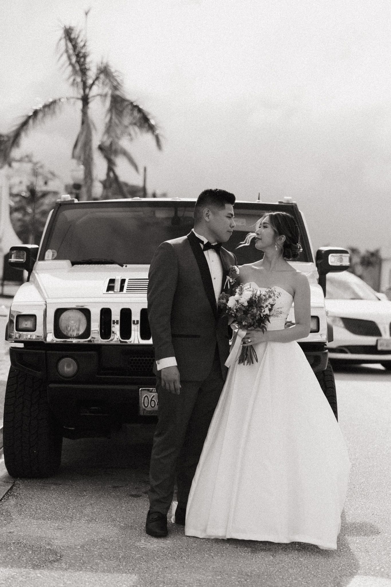 Black and white photo of a bride and groom posing in front of a white Hummer on their wedding day.