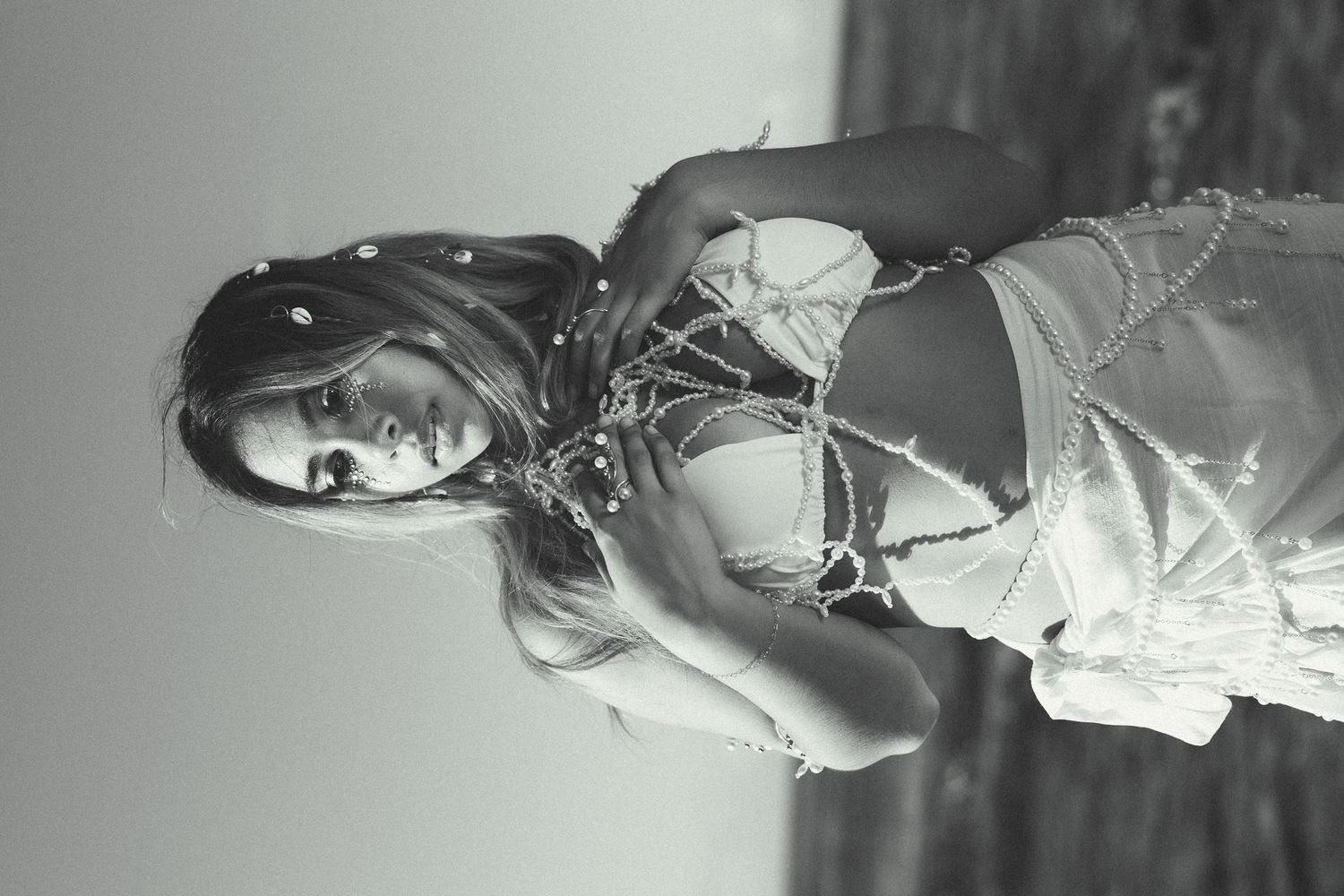 Black and white portrait of a woman in a decorative beaded outfit posing outdoors.