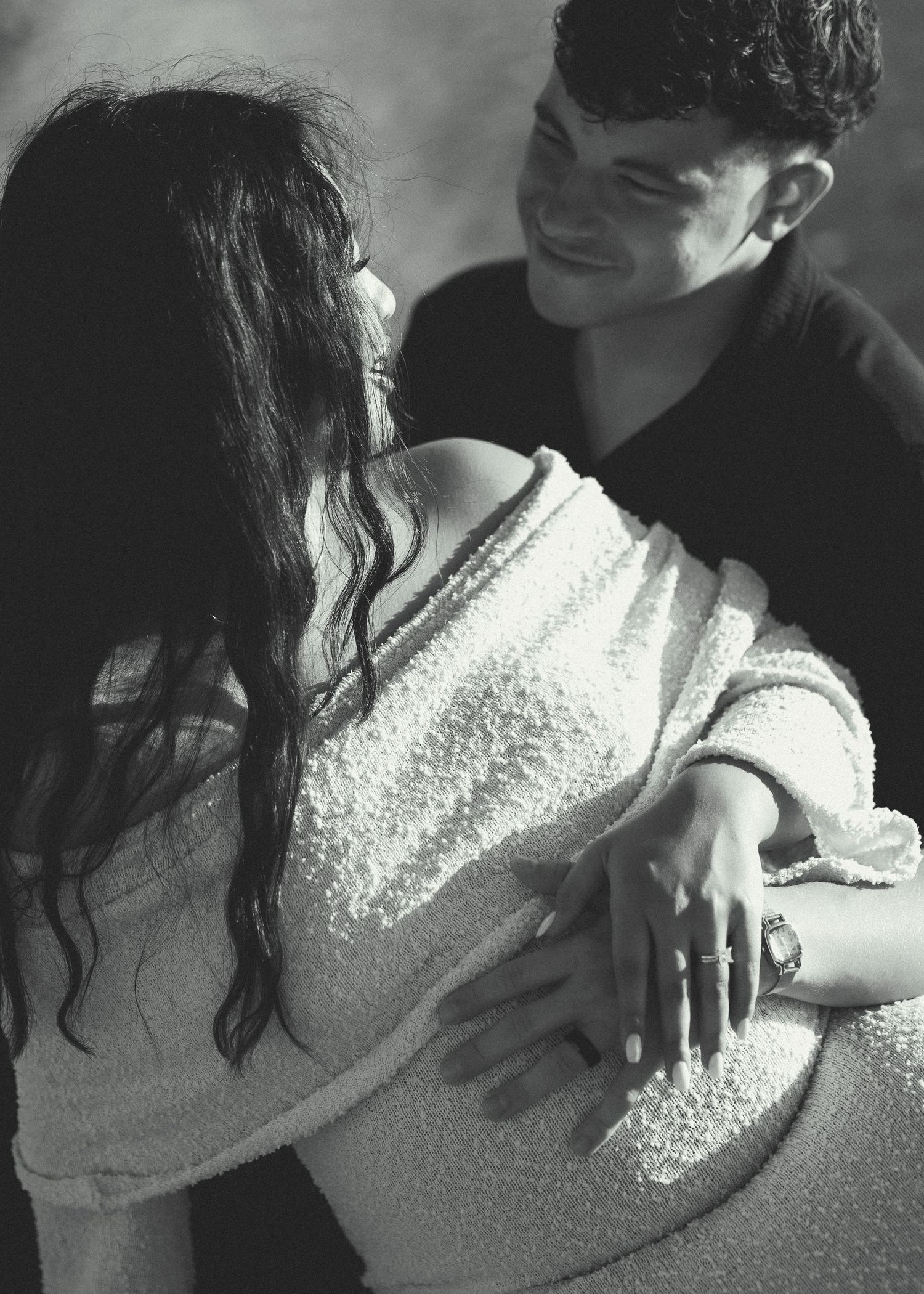 Black and white photo of a smiling man embracing a woman from behind, both sharing a tender romantic moment.