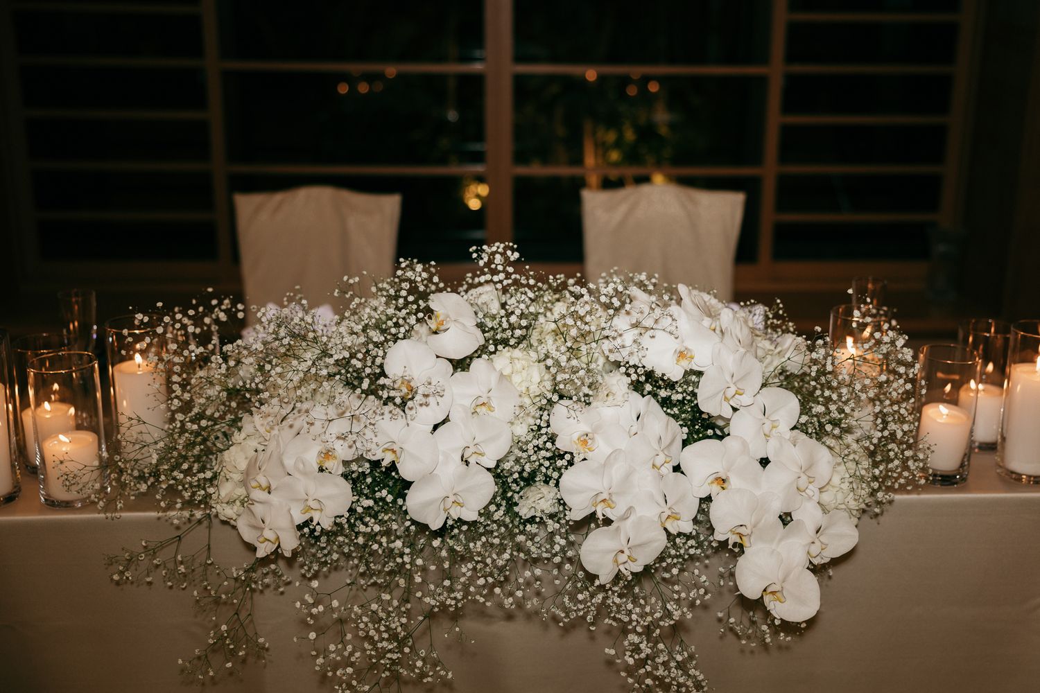 White orchids and baby's breath centerpiece with candles on a wedding reception table.