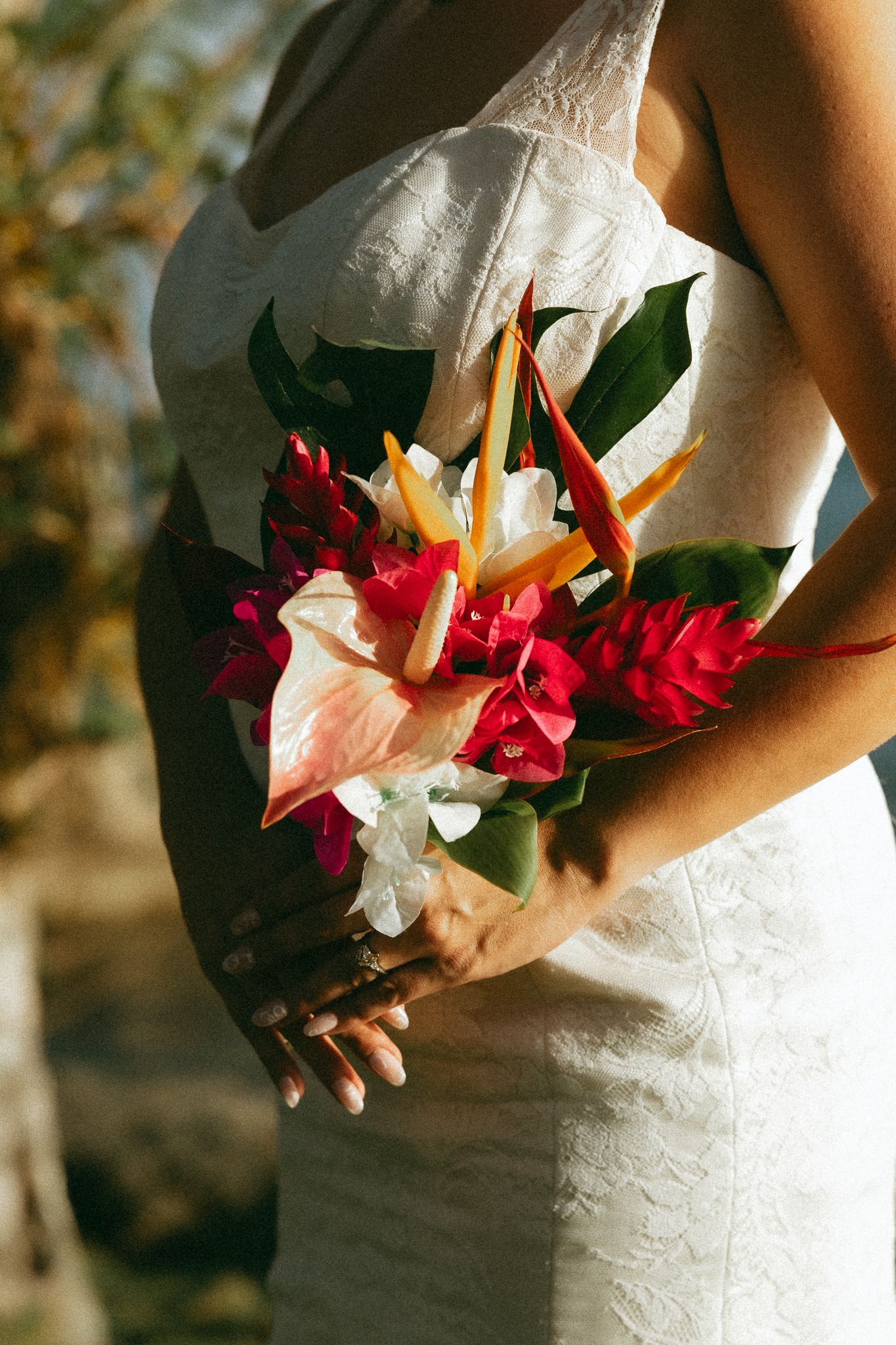 Bride in white lace dress holding tropical wedding bouquet with bird of paradise, anthurium, and red ginger flowers.