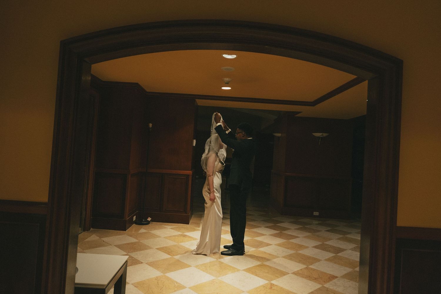 Couple sharing a romantic dance in an elegant dimly lit hallway with checkered floors.