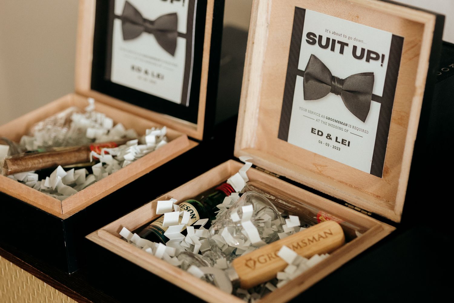 Groomsmen gift boxes with bow tie signs, cigars, and wine bottles labeled 