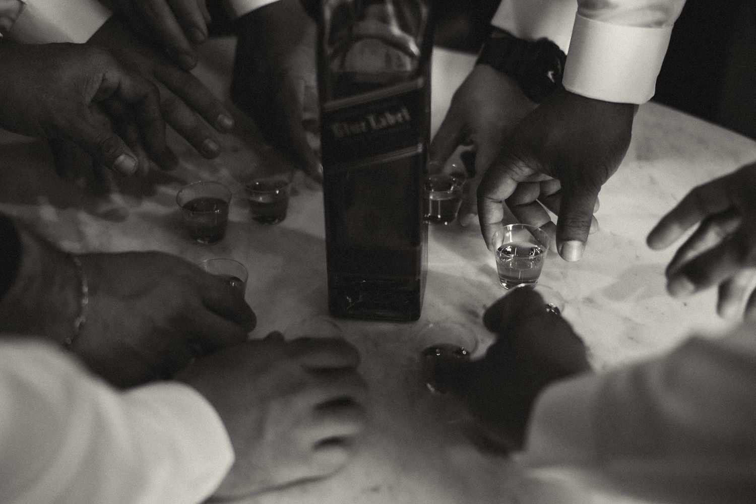 Black and white photo of men pouring whiskey shots from a Blue Label bottle at a gathering.