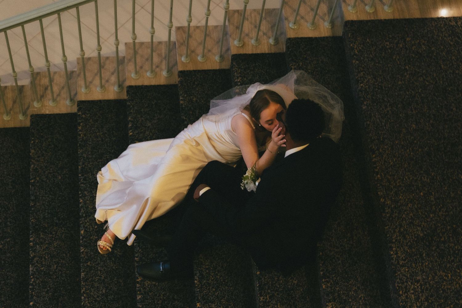 Bride and groom sharing a romantic kiss while lying on granite stairs in wedding attire.