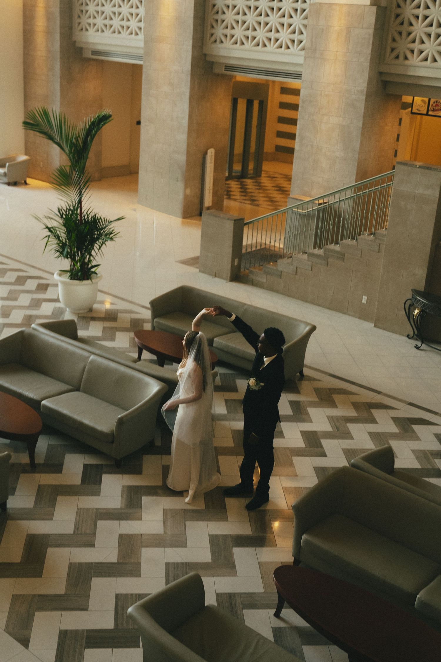 Aerial view of bride and groom dancing in an elegant hotel lobby with chevron patterned floors.