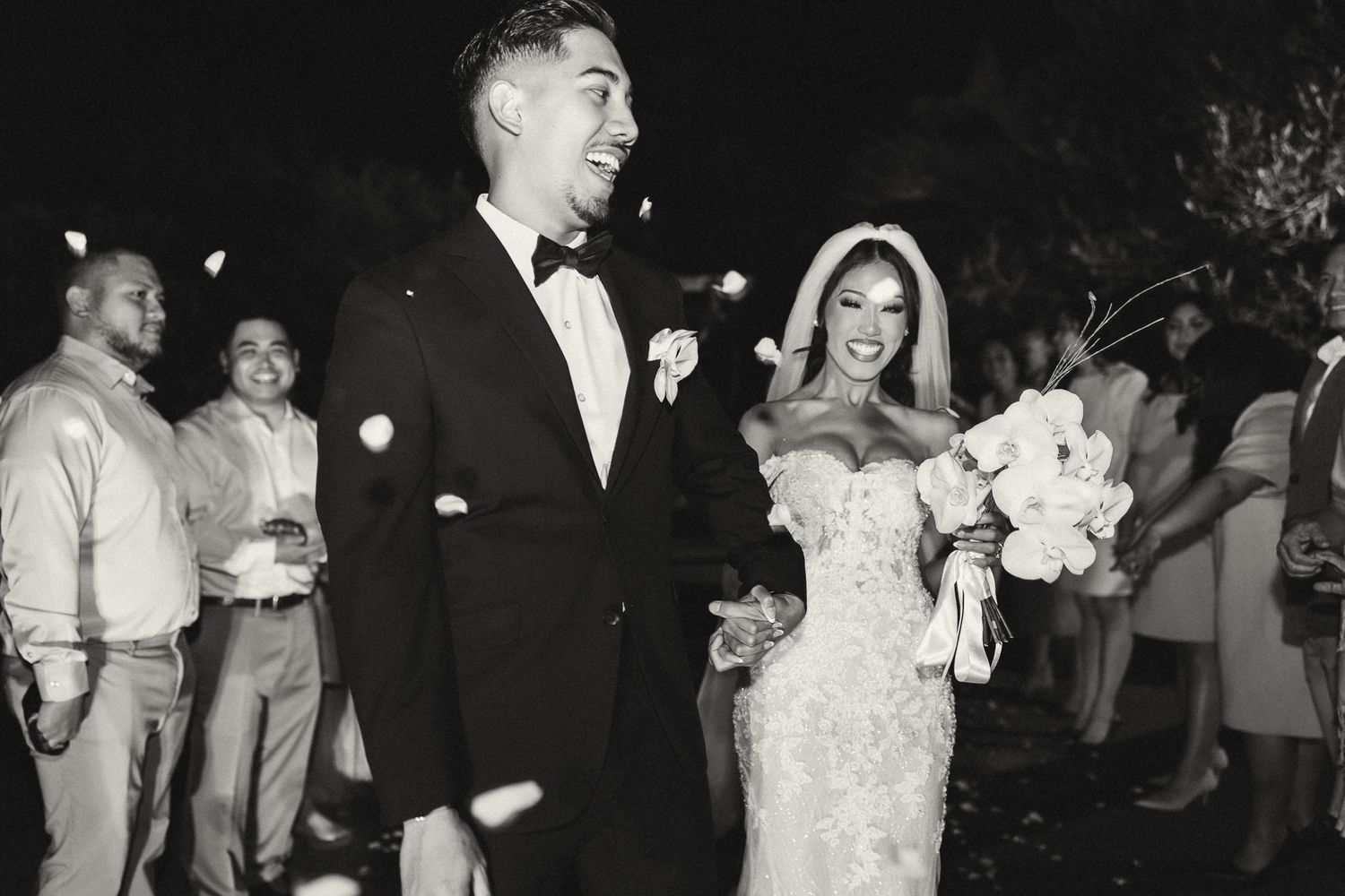 Black and white photo of a joyful bride and groom walking together after their wedding ceremony.