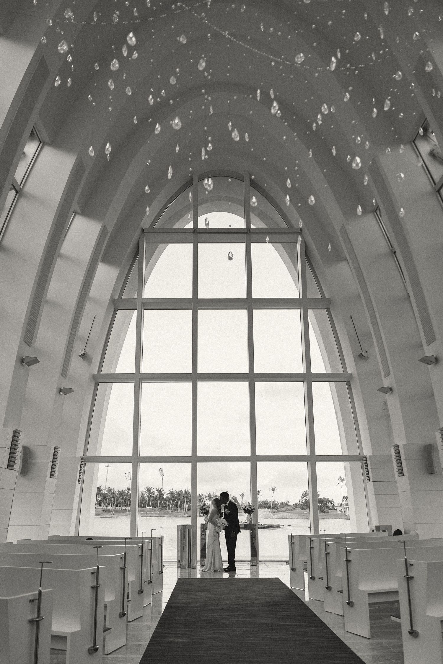 Black and white photo of a bride and groom standing at the altar of a stunning chapel with arched windows.