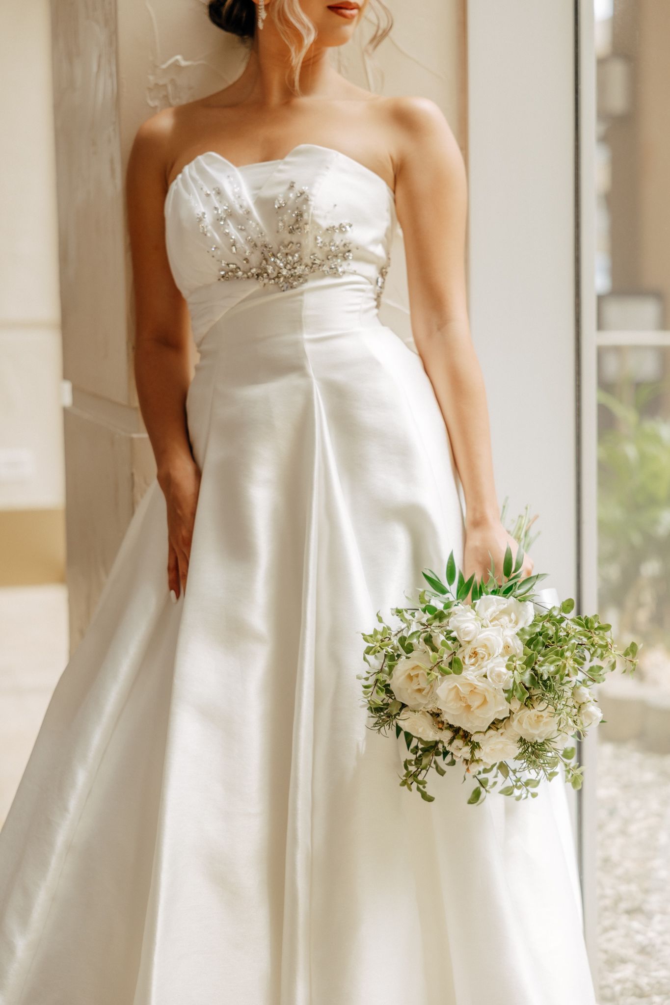 Bride in strapless satin A-line wedding gown holding white and green bridal bouquet.