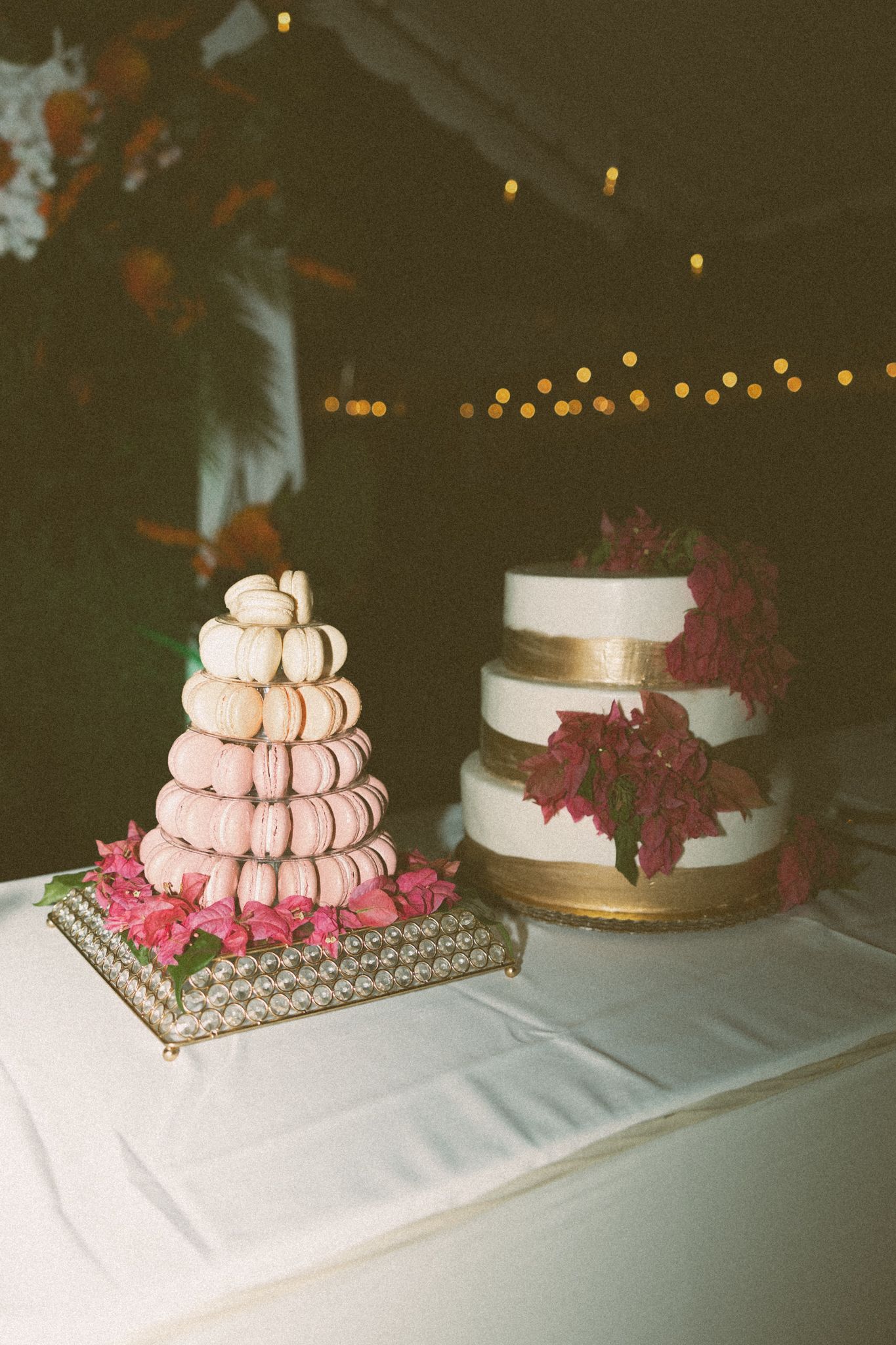 Elegant wedding dessert table featuring a macaron tower with pink flowers and a two-tier white cake with red floral decorations.
