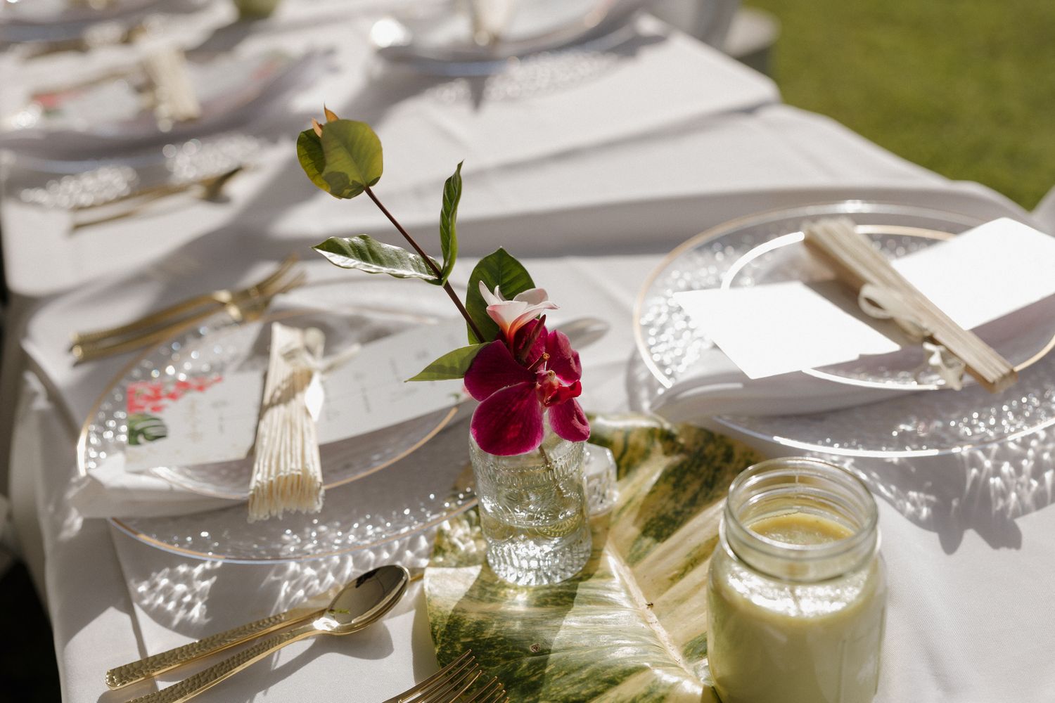 Elegant wedding table setting with white linens, gold cutlery, and a small vase with a red flower centerpiece.