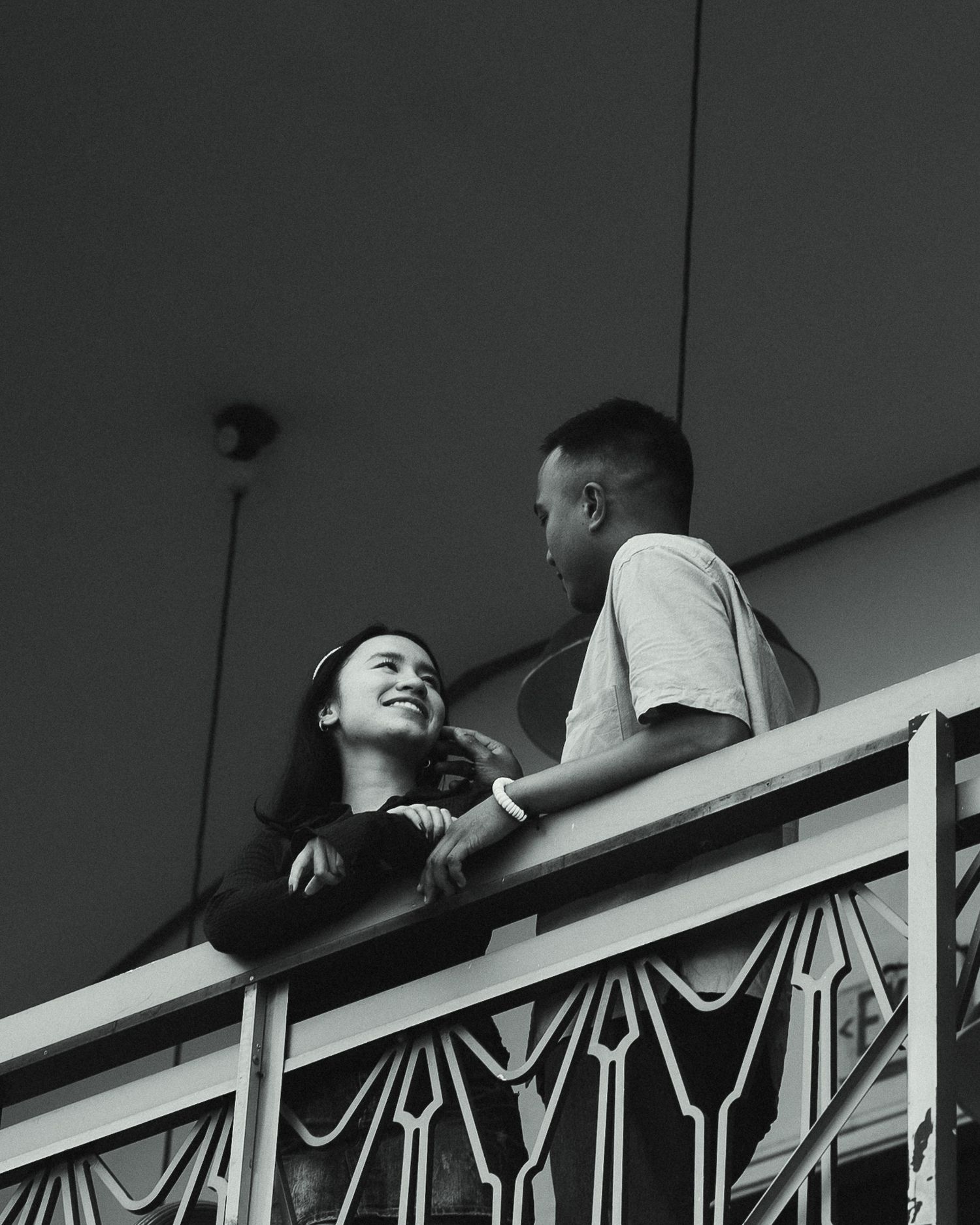 Black and white photo of a smiling couple on a balcony, sharing a joyful moment together.