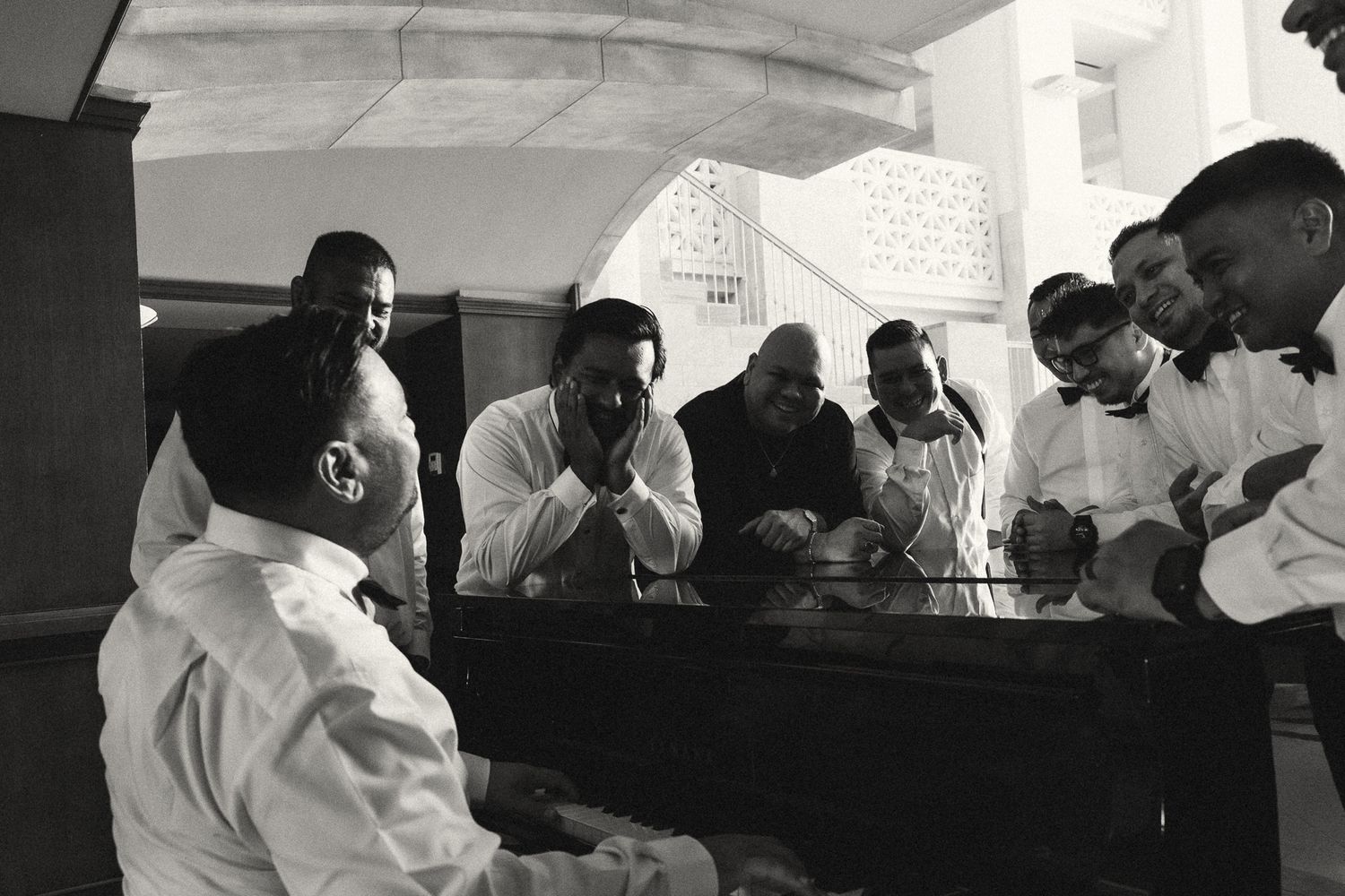 Black and white photo of a group of men in white shirts gathered around a table in conversation.