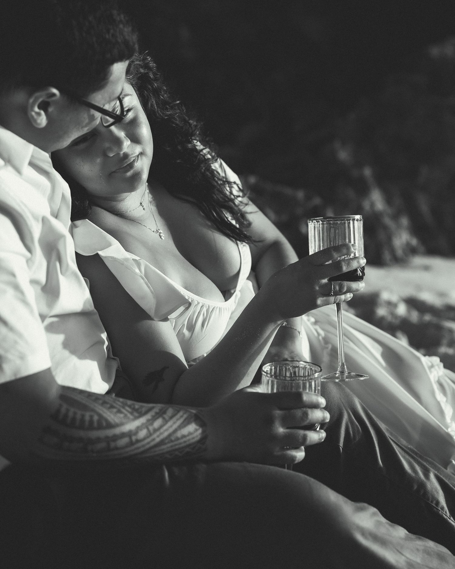 Black and white photo of a couple relaxing together, sharing wine glasses in a romantic outdoor setting.