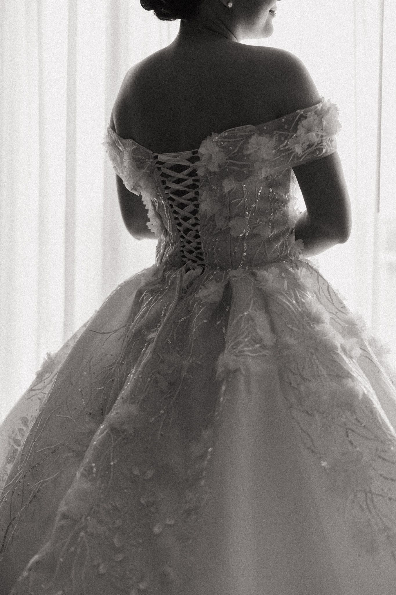 Black and white rear view of bride in off-shoulder corset wedding gown with floral embellishments.