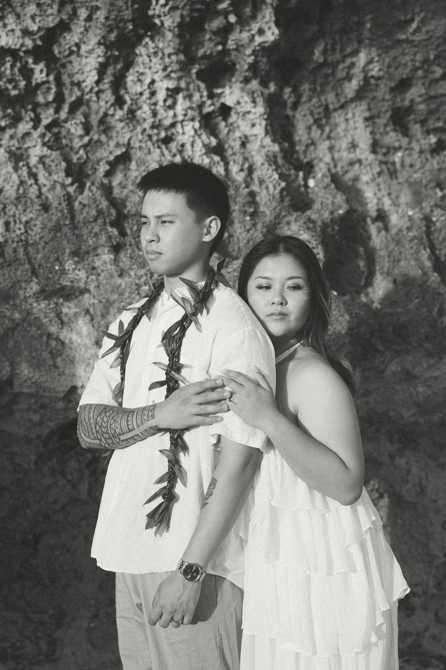Black and white photo of a couple in white attire embracing against a rocky background.