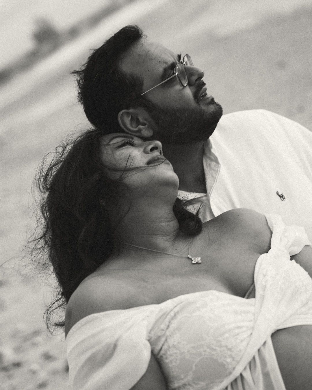 Black and white photo of a couple in white outfits, woman leaning back on man outdoors.