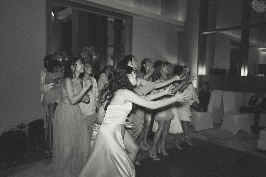 Black and white photo of bridesmaids dancing and celebrating at a wedding reception in an elegant venue.
