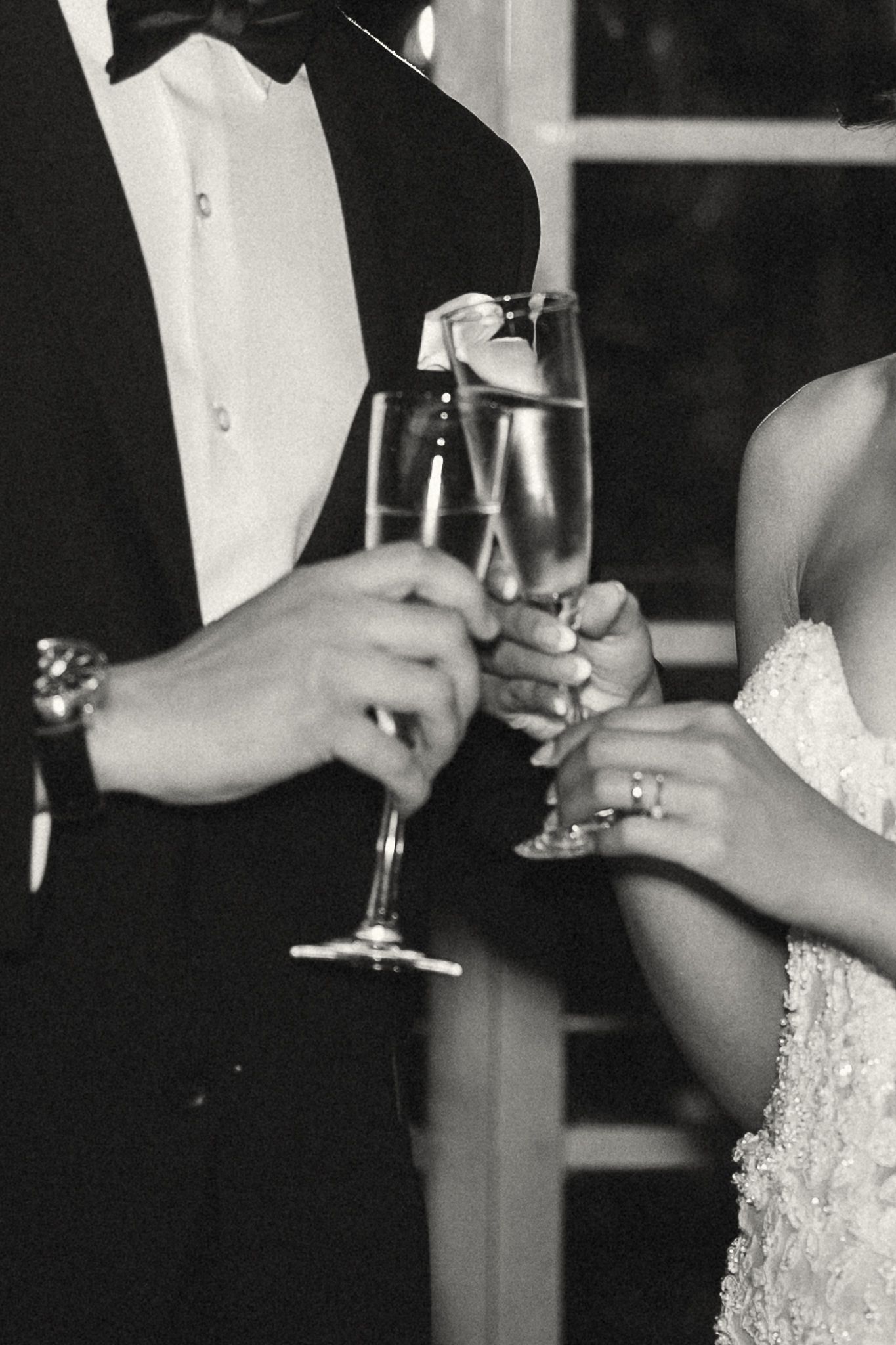 Bride and groom clinking champagne flutes in elegant black and white wedding toast photo.