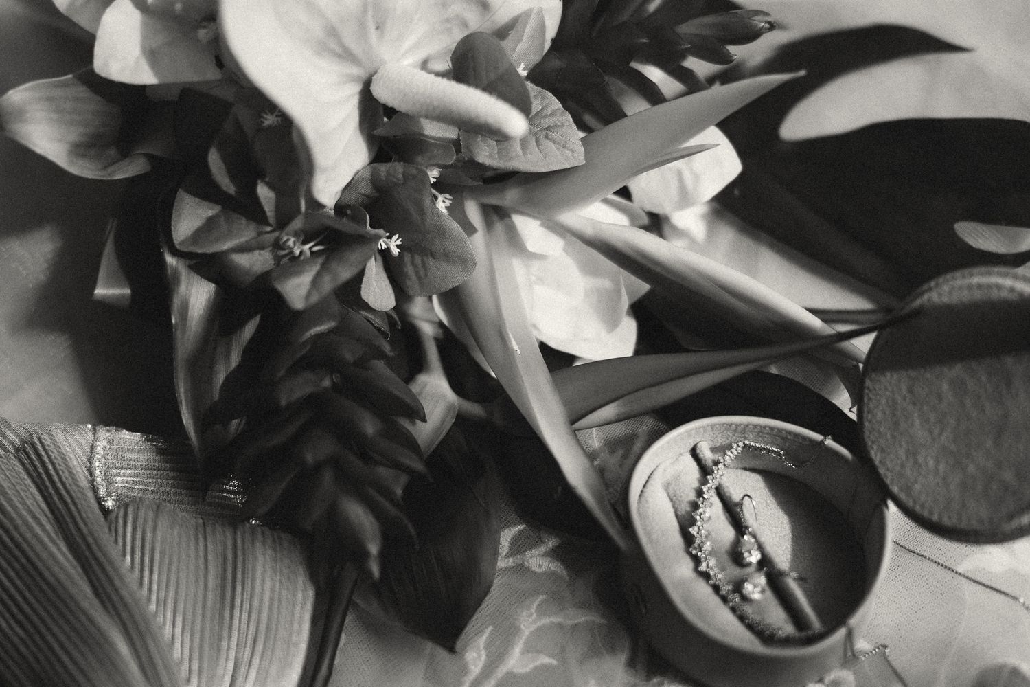 Black and white still life photo of tropical leaves, flowers, scissors, and a small dish with jewelry.