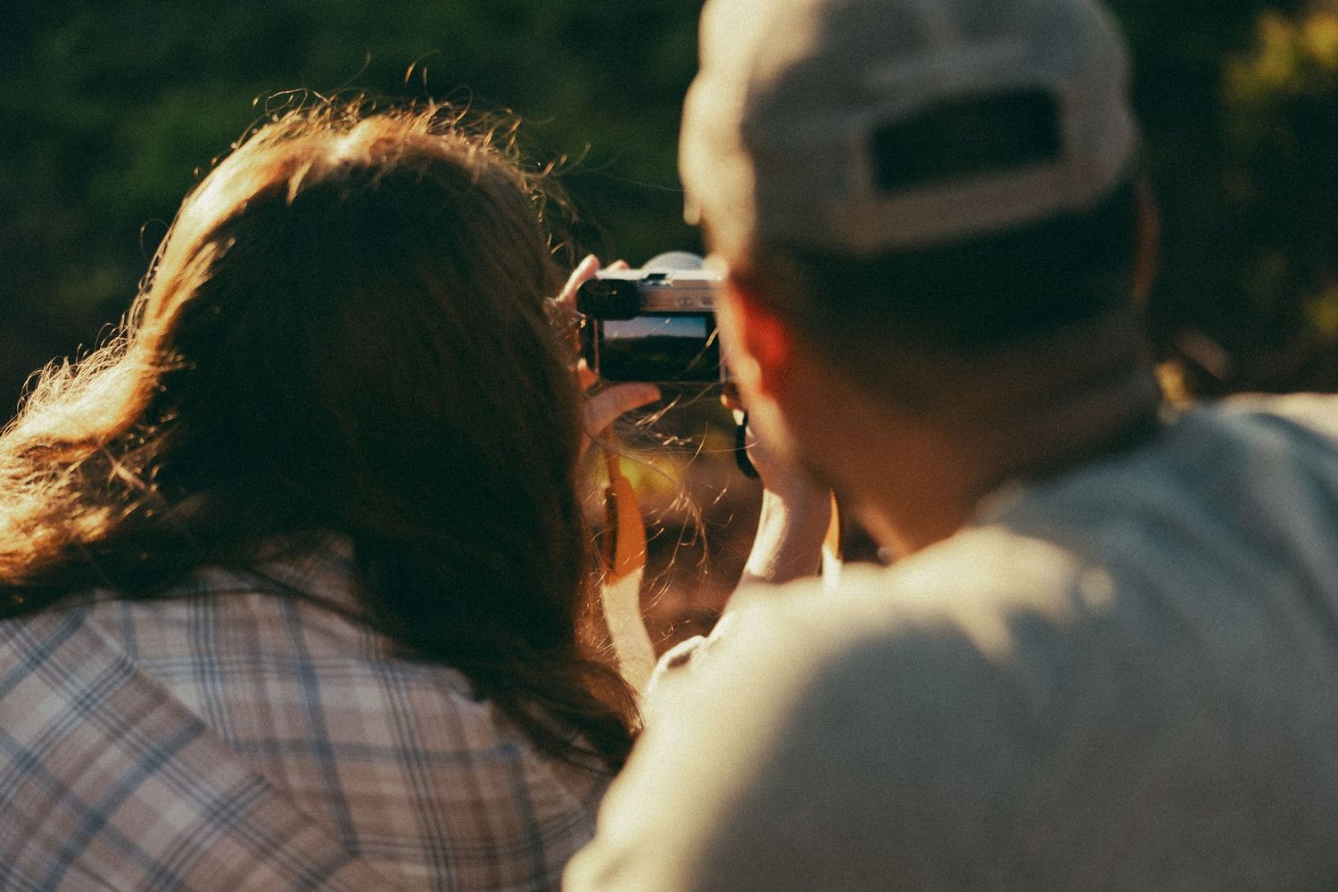 Couple sharing a moment while looking through a vintage camera outdoors in warm sunlight.