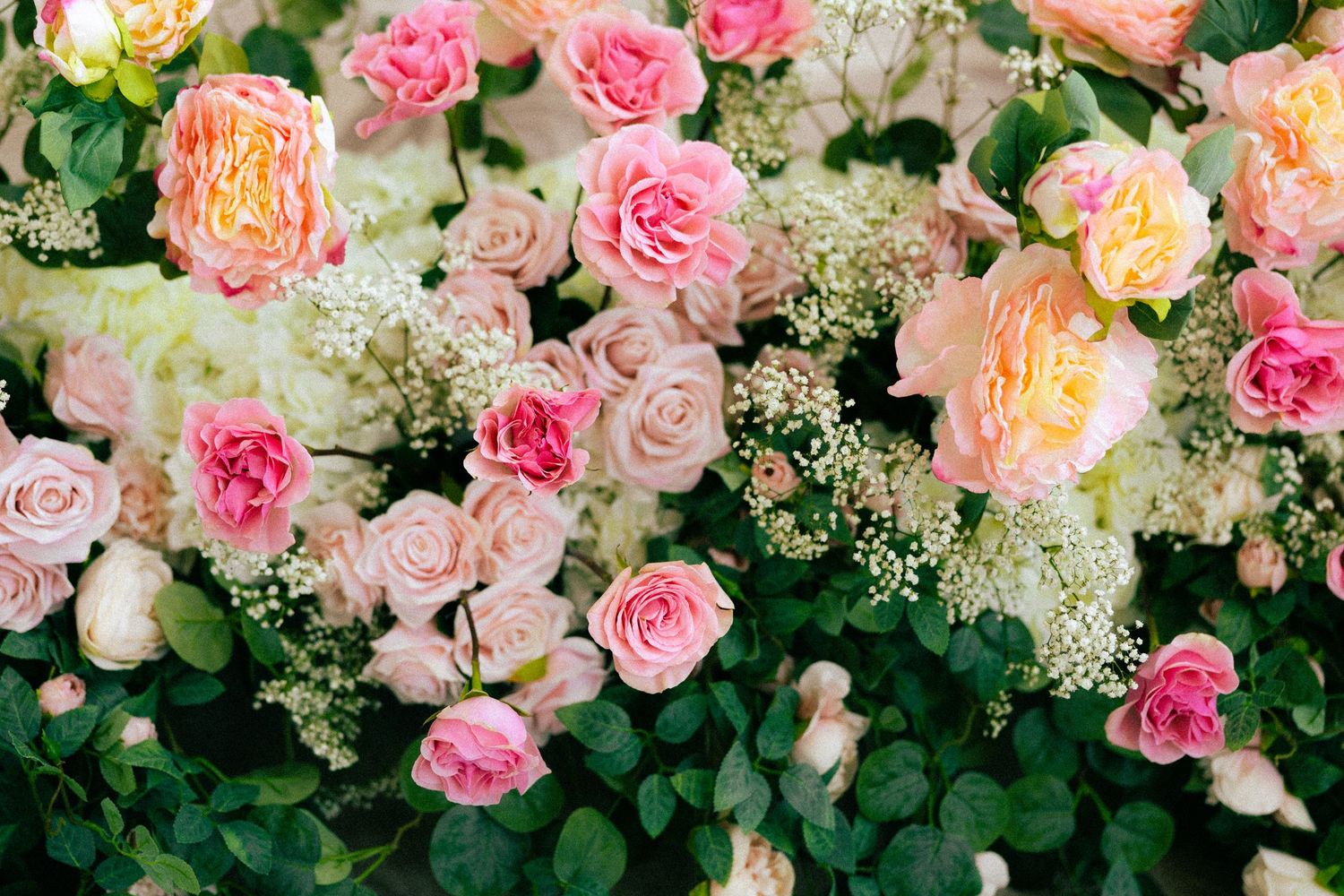 Lush floral arrangement featuring pink, peach, and cream roses with baby's breath and green foliage.